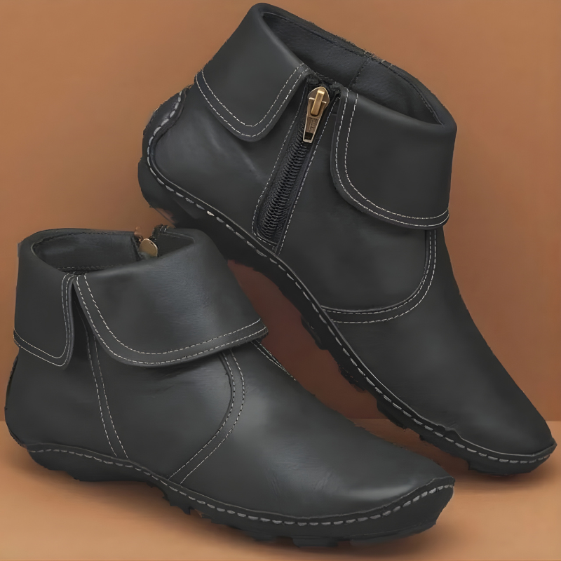 Black ankle boots arranged with one raised behind the other, showing the foldover collar, contrasting edge stitching, side zip, and rugged sole.