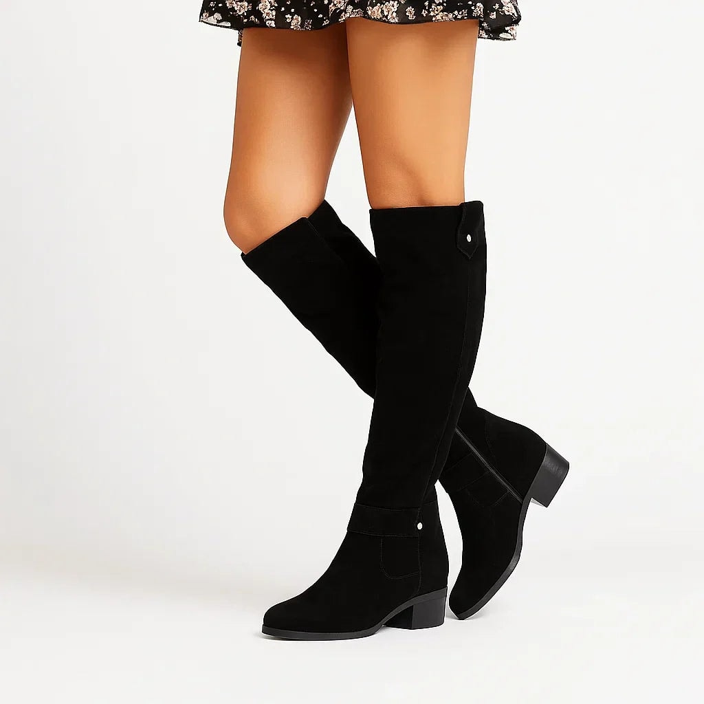 Black knee-high boots styled with a floral skirt, featuring side zippers, ankle straps, rounded toes, and low block heels.