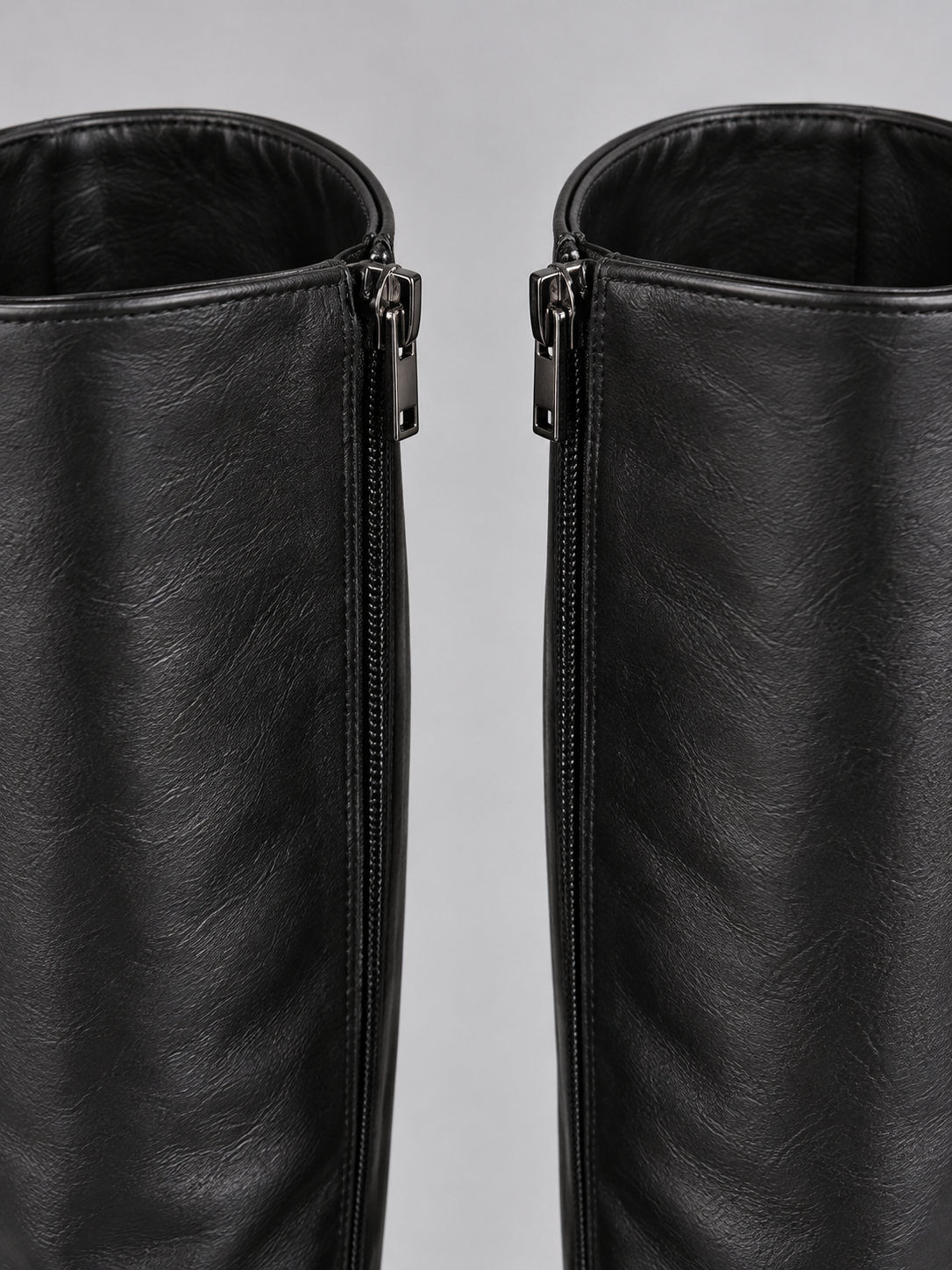 Close-up of the upper shafts of the black knee-high boots, highlighting the side zip fastenings and smooth profile.