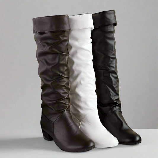 Woman wearing knee high slouchy boots with round toe paired with distressed jeans on a sandy outdoor surface._3