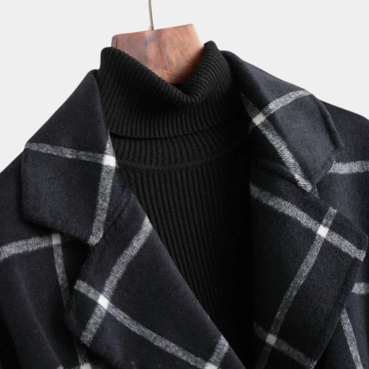 Close-up of the black plaid coat on a hanger, emphasizing its broad notched lapels and single-breasted front over a dark turtleneck.