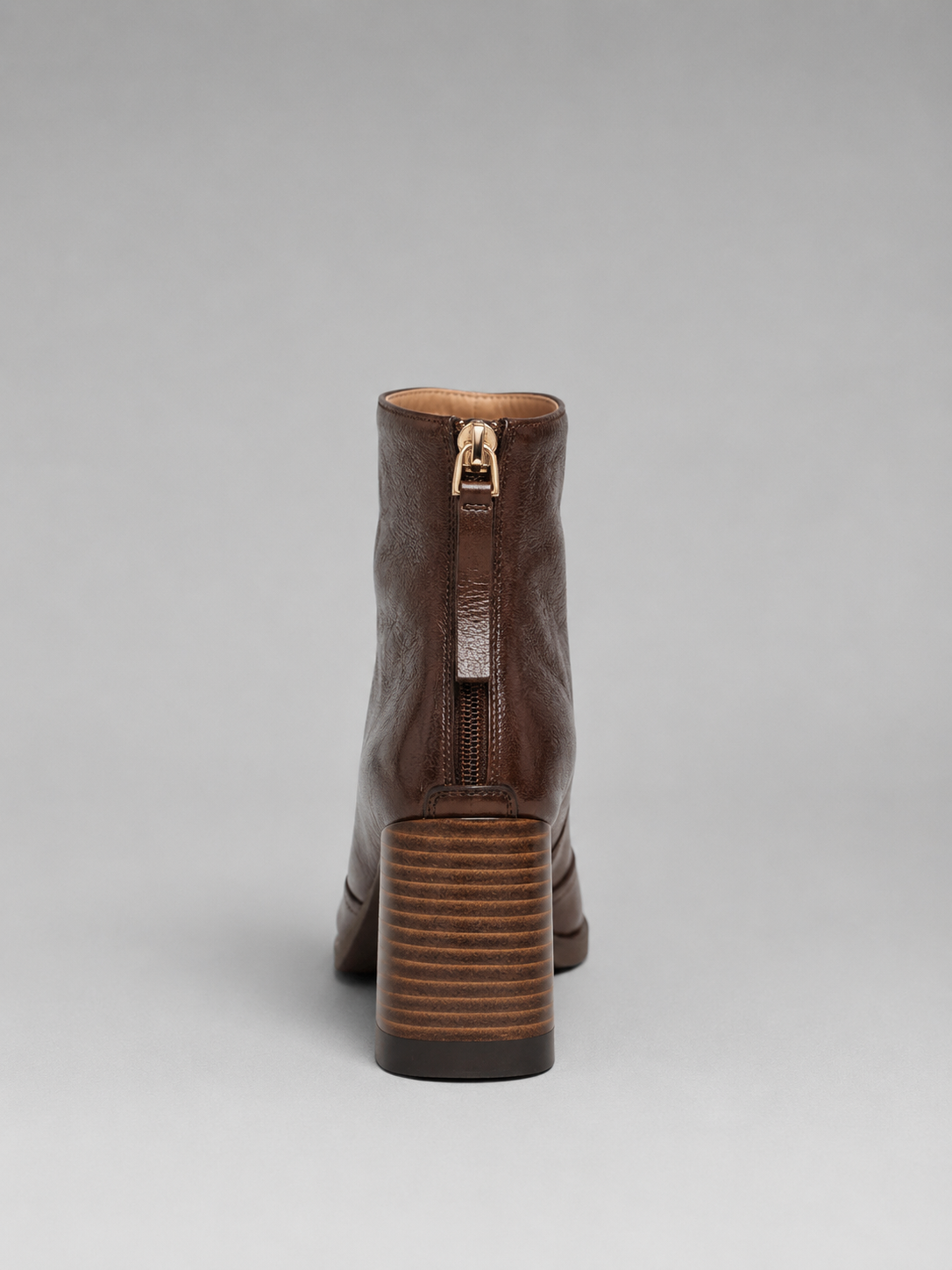 Rear view of a brown ankle boot showing the centered back zip and horizontally ridged block heel.