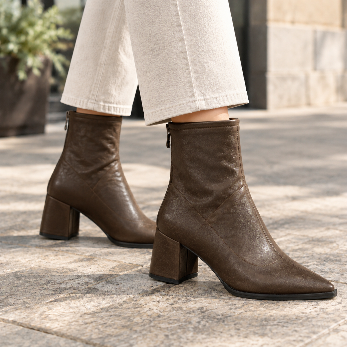 Brown ankle boots highlighting the pointed toes, structured block heels, and side zipper detail beneath cropped cream trousers.