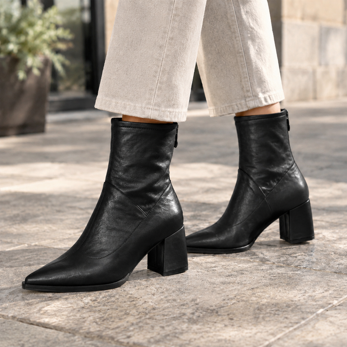 Black pointed-toe ankle boots with fitted ankle shafts and sturdy block heels, styled with cropped cream trousers.