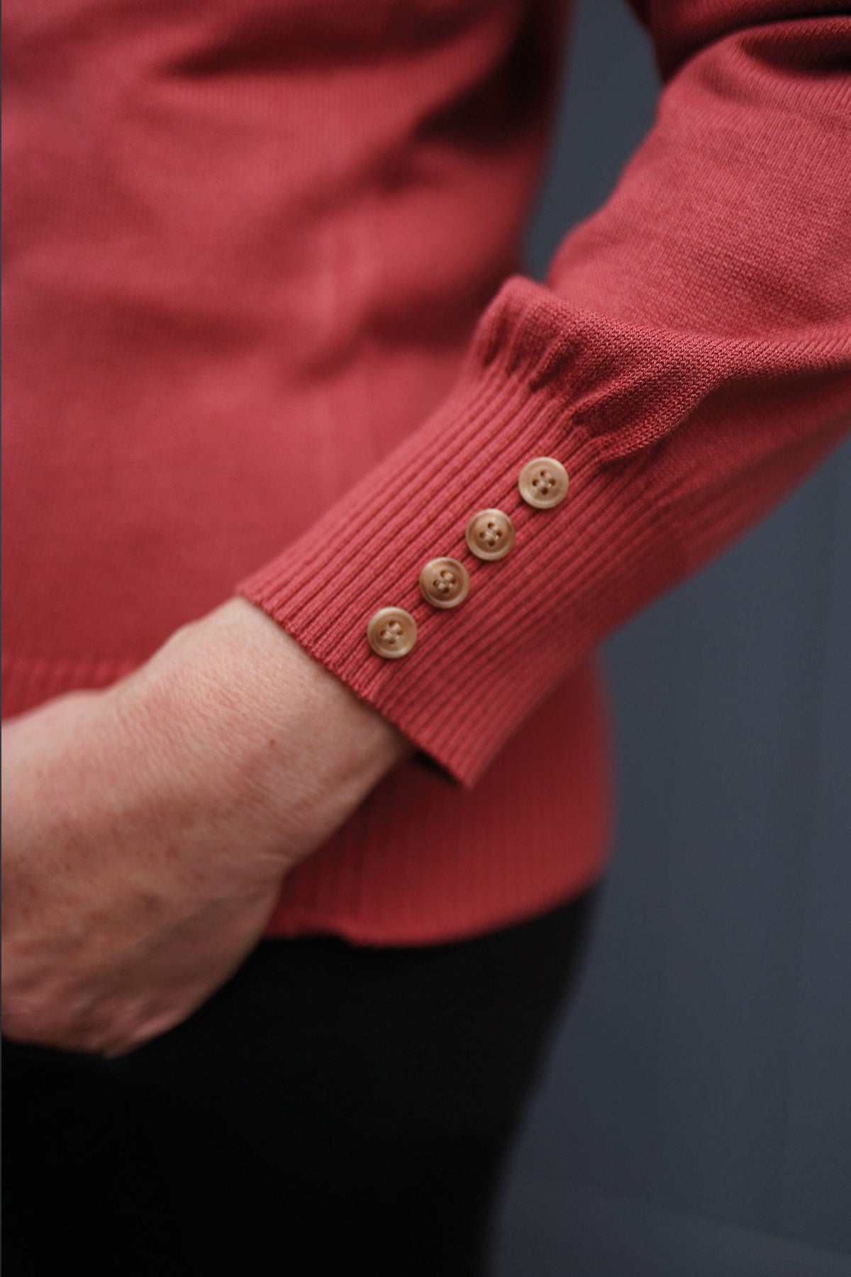 Woman wearing a long sleeve knitted jumper with a funnel collar, buttons along one side of the neck and buttoned ribbed cuffs._10