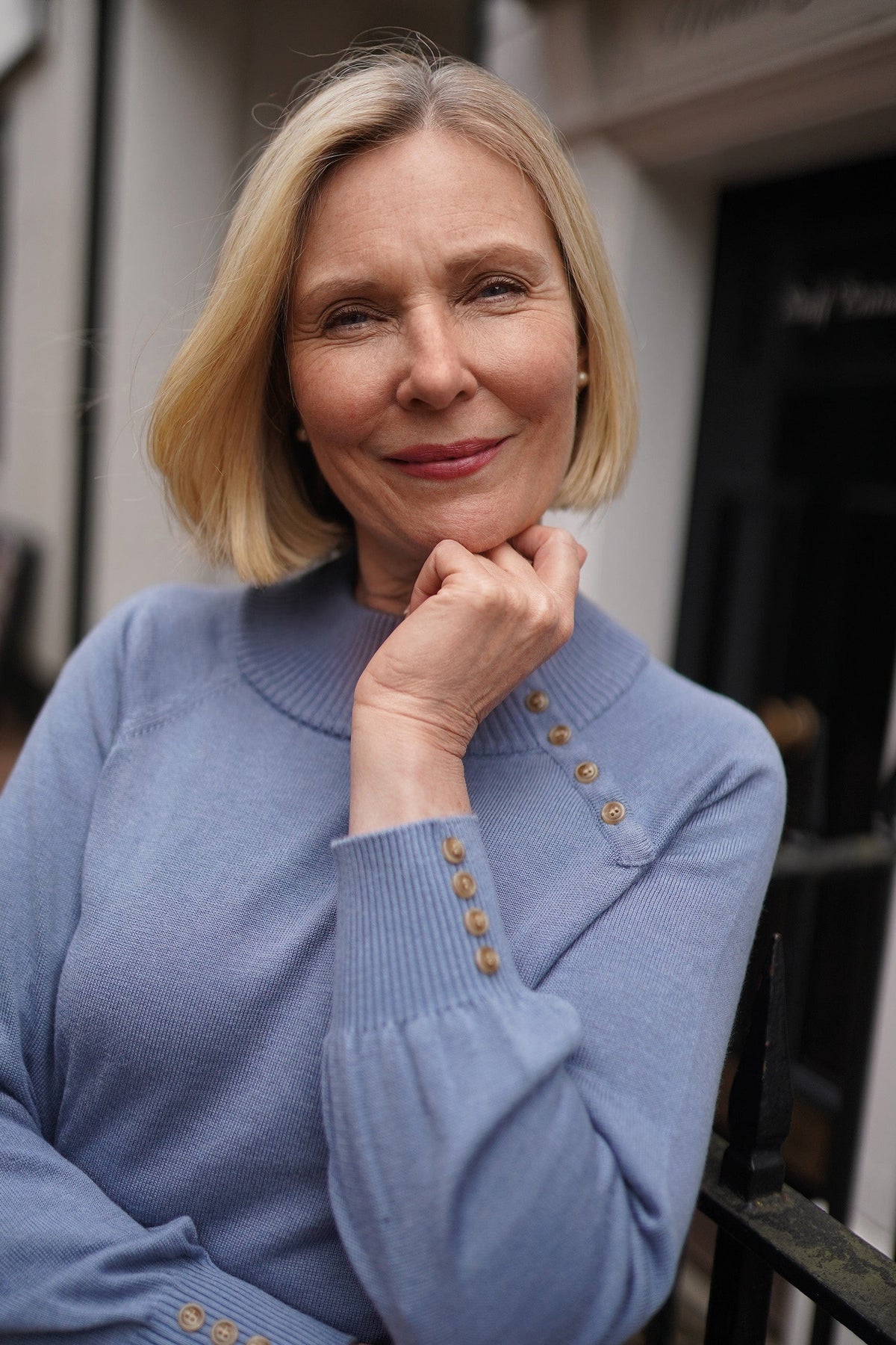 Woman wearing a long sleeve knitted jumper with a funnel collar, buttons along one side of the neck and buttoned ribbed cuffs._11