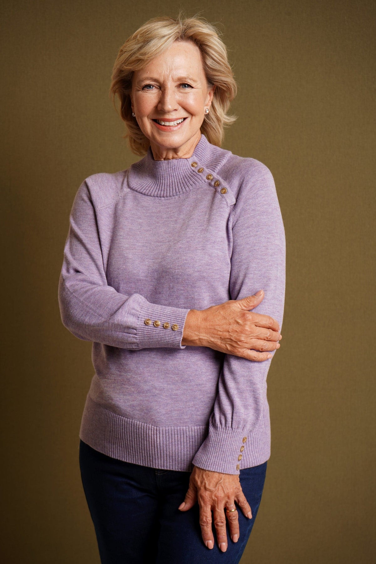 Woman wearing a long sleeve knitted jumper with a funnel collar, buttons along one side of the neck and buttoned ribbed cuffs._3
