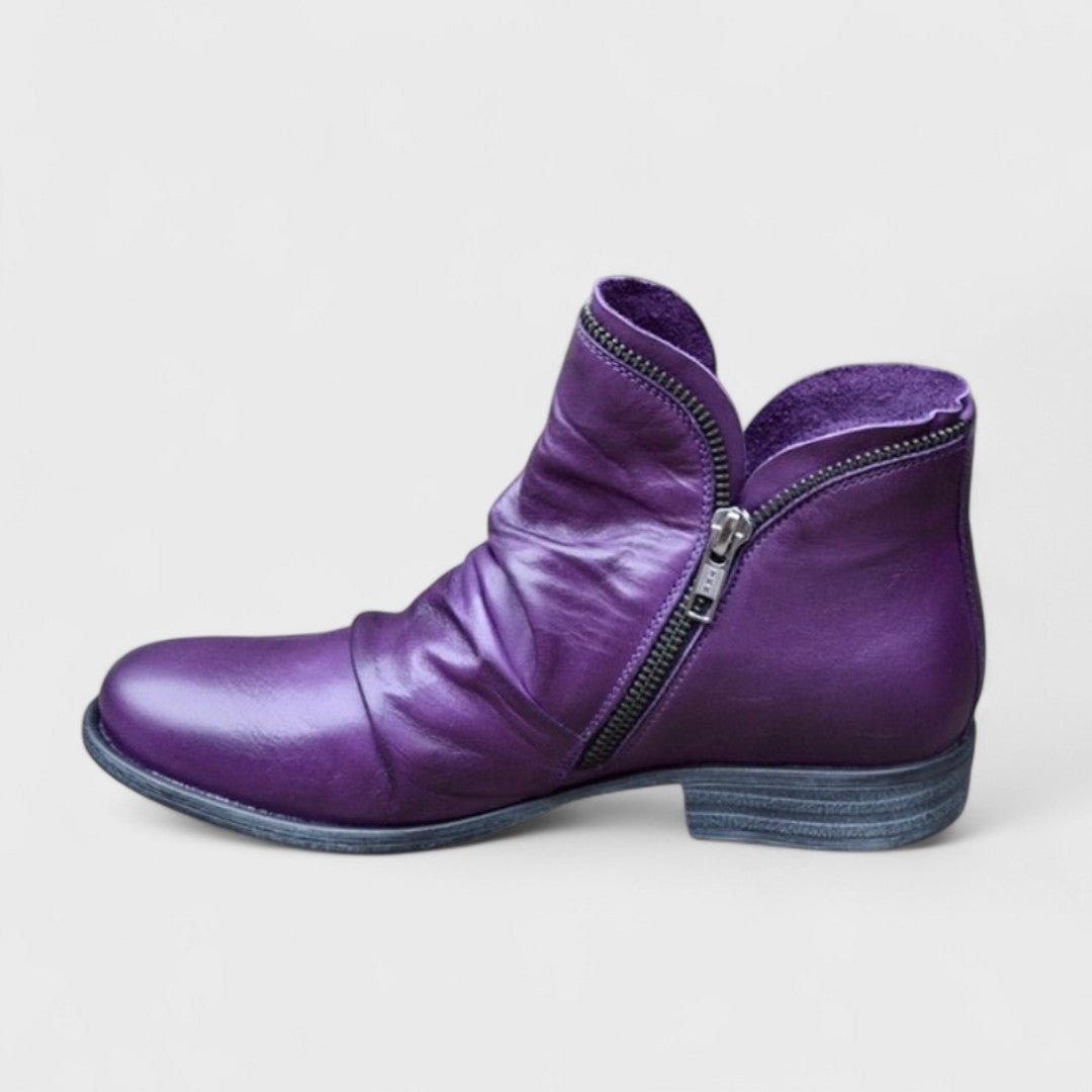 Purple ankle boot shown in side profile with a curved zip closure, gathered front detailing, rounded toe, and low block heel.