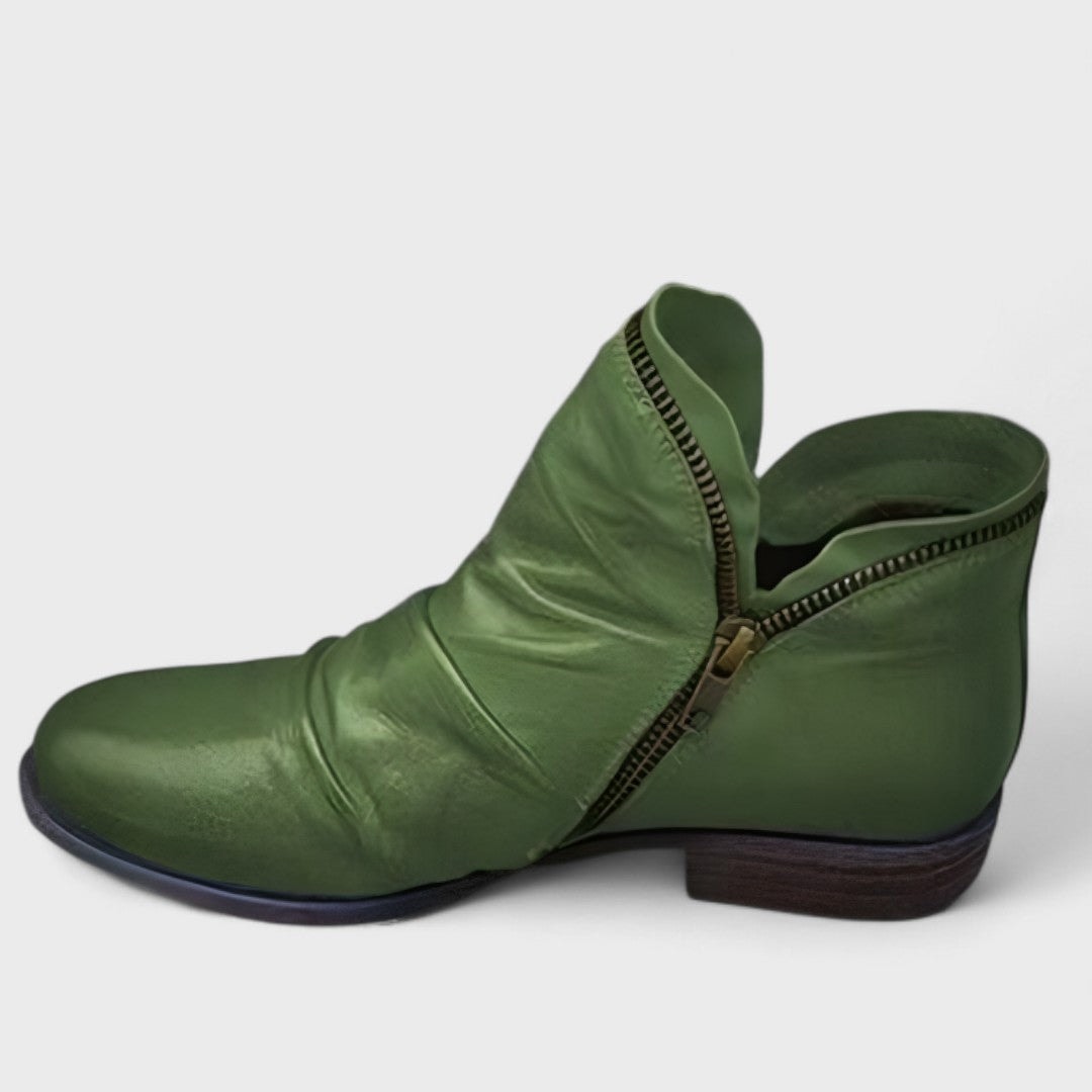 Green ankle boot viewed from the side, showing its curved zip closure, gathered front, rounded toe, and dark low block heel.