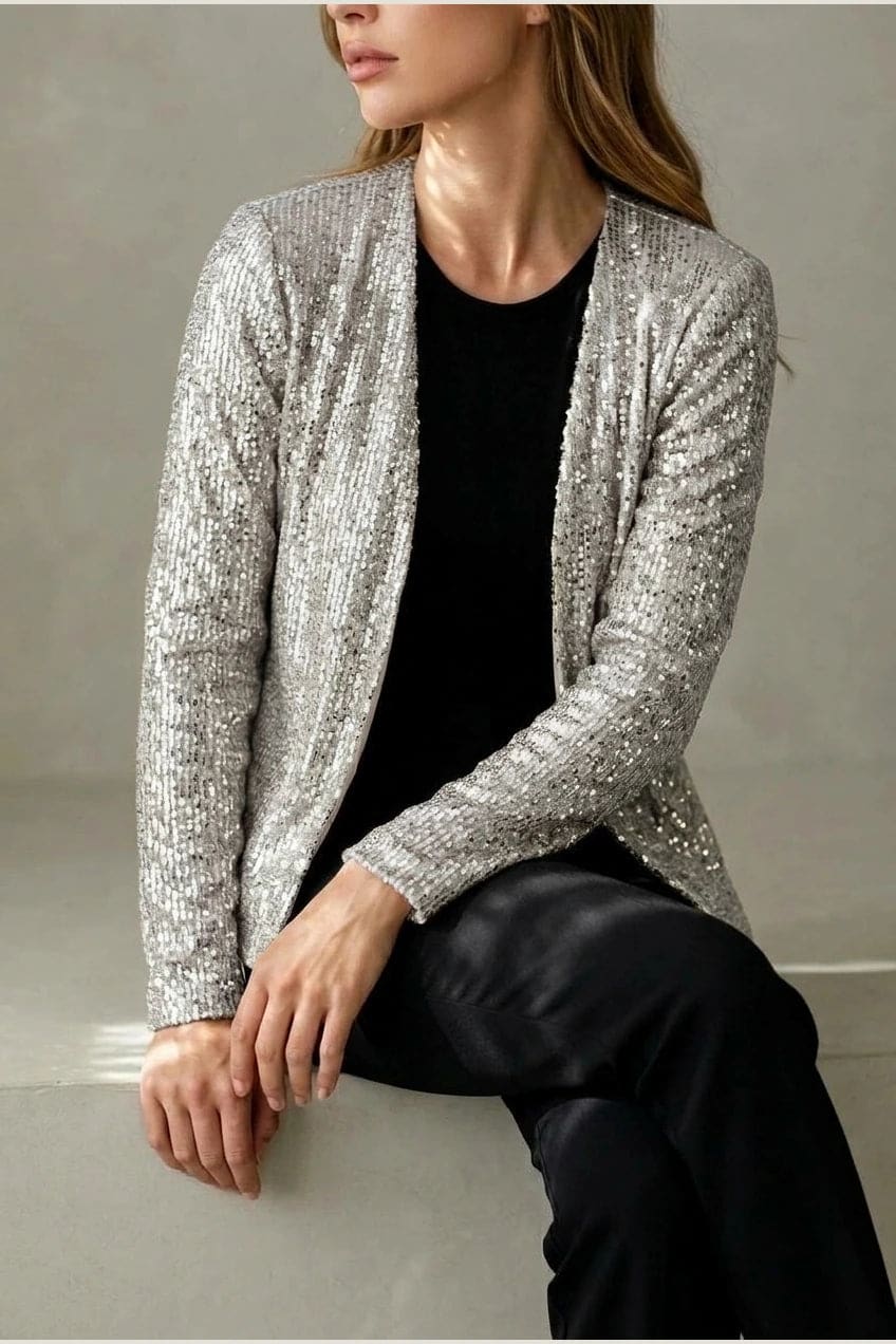 Model wearing an open-front cropped sequin jacket with long sleeves and structured shoulders over a tank top and tailored trousers._11
