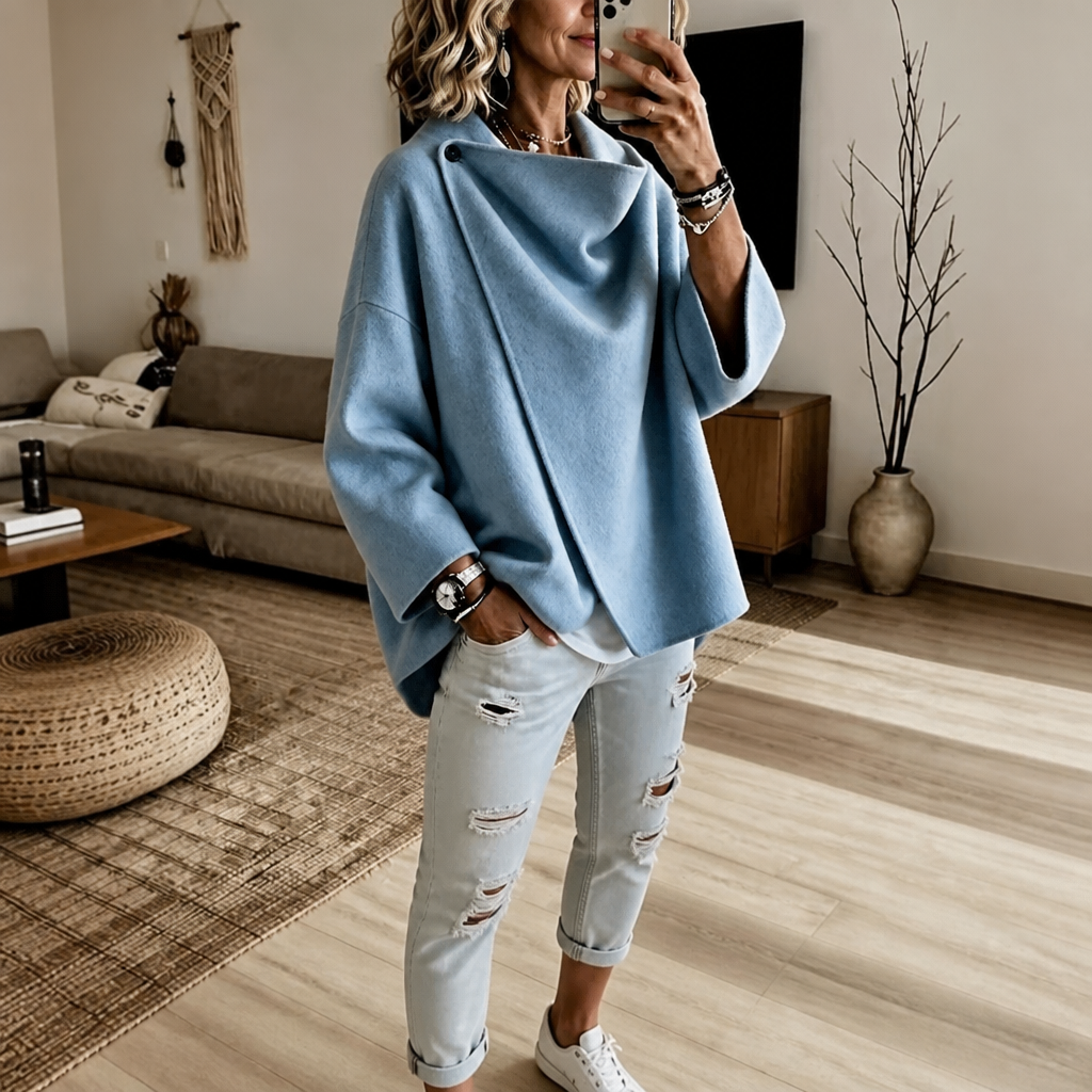 Mirror view of the asymmetric cape jacket in blue, showing the draped collar and wide three-quarter sleeves.