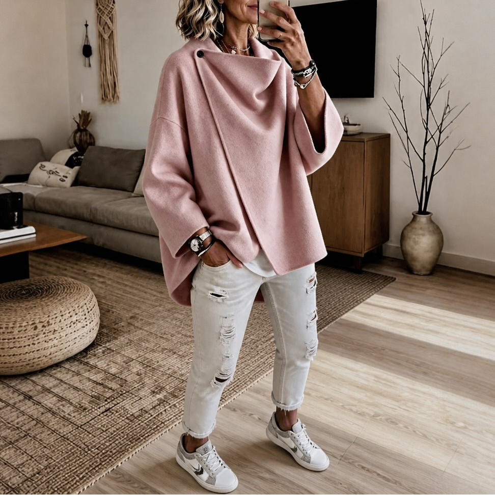 Mirror view of the asymmetric cape jacket in pink, paired with white jeans and sneakers.