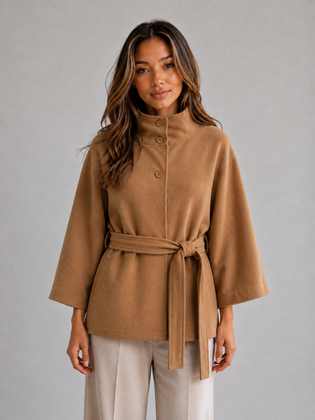 Front view of a camel cape-style jacket with a stand collar, button front, wide three-quarter sleeves, and a tied waist belt.