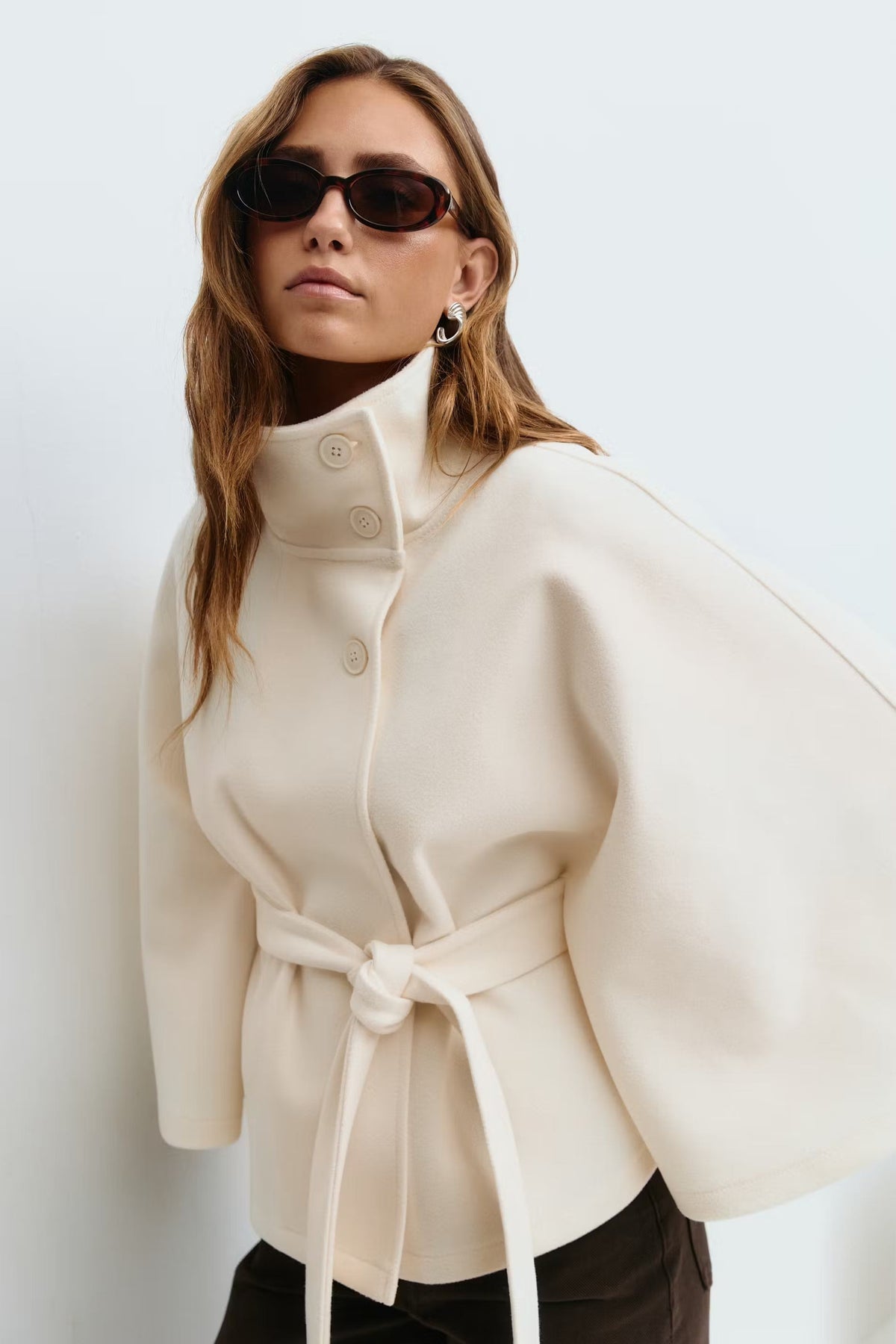 Ivory belted cape jacket styled on a model, showing the structured stand collar, front buttons, and tied waist.