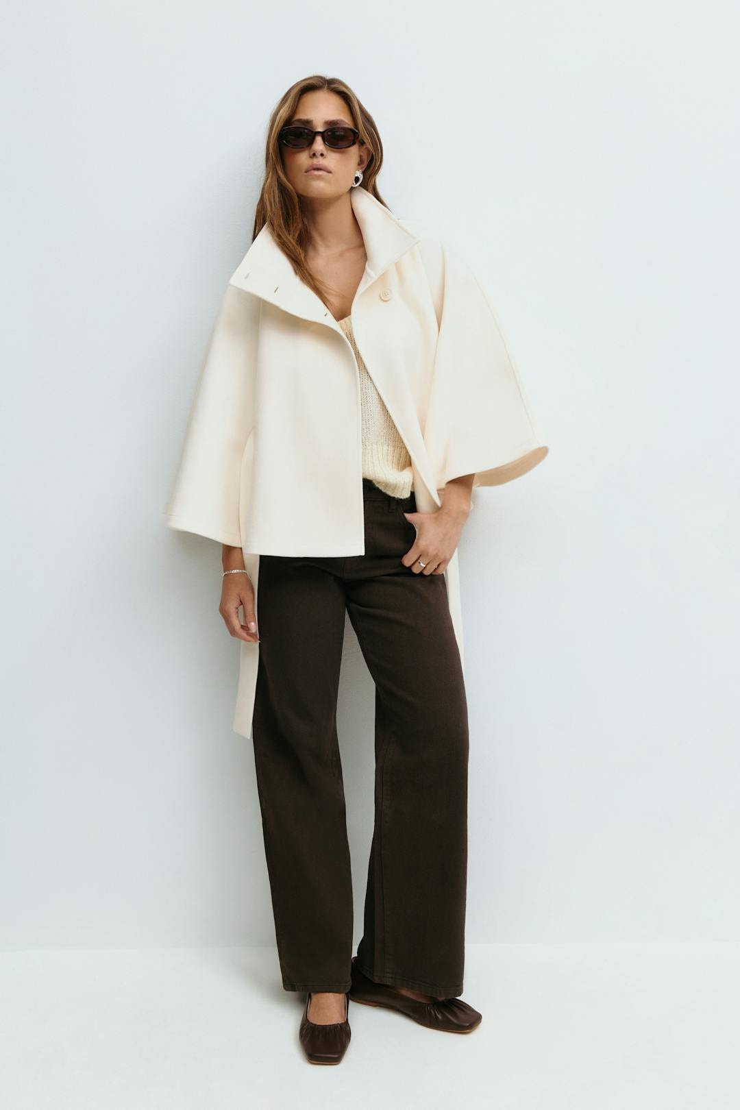 Full-length view of the ivory cape jacket worn open over a top, showing its short flared silhouette and wide sleeves.