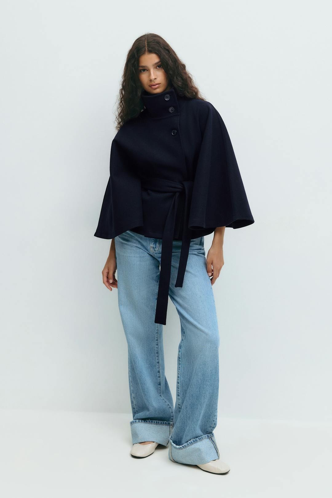 Full-length view of the navy cape jacket styled with jeans, showing the cinched waist and flowing sleeves.