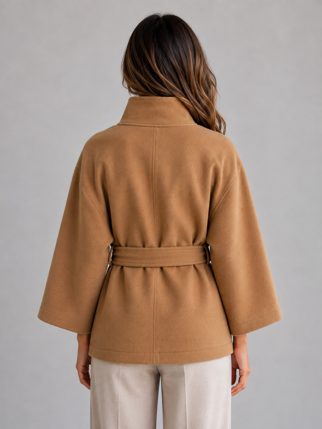 Back view showing the camel jacket’s cape silhouette, high stand collar, wide sleeves, and belt cinched across the waist.