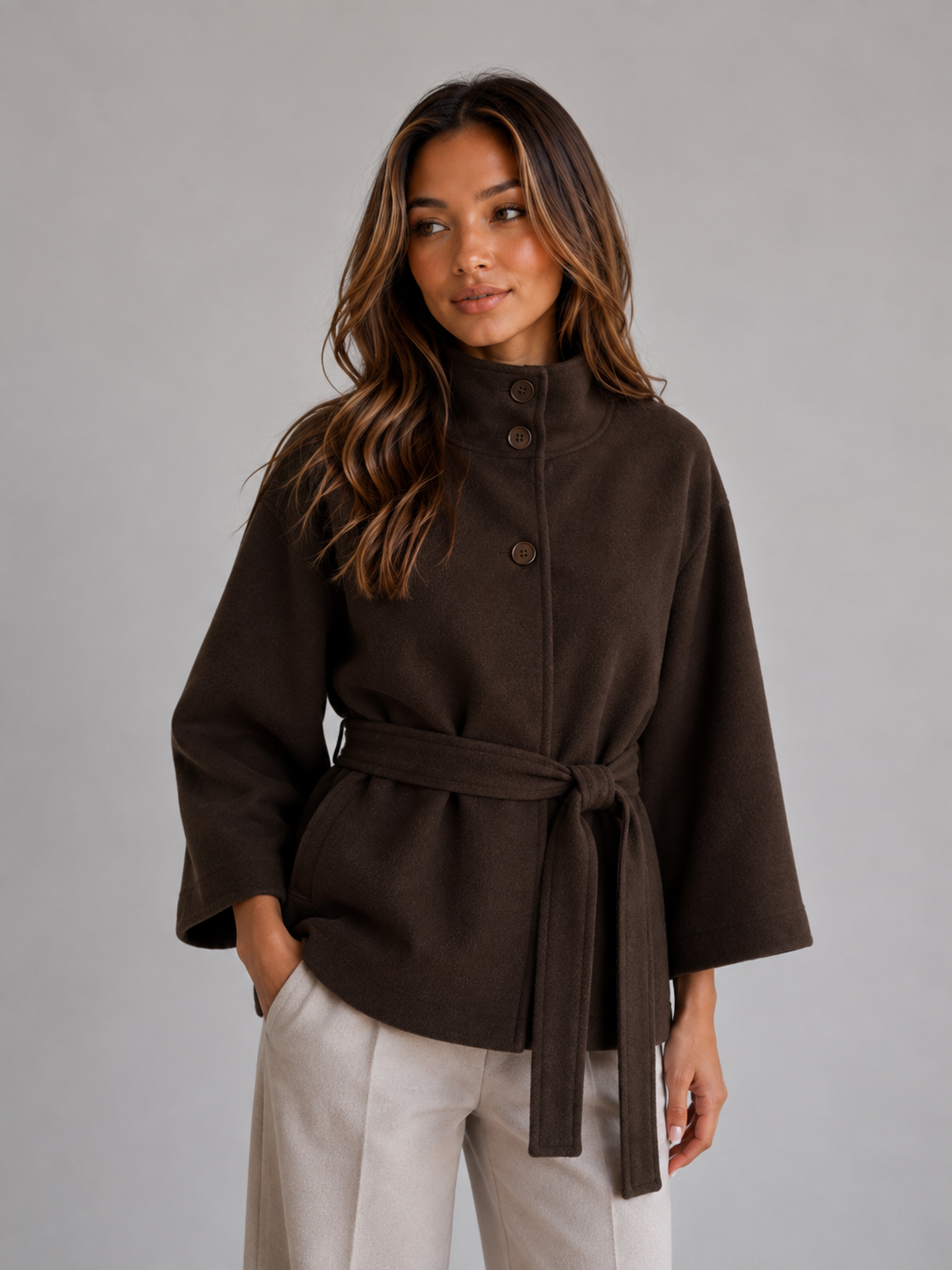 Front view of the cape jacket in dark brown, styled with a buttoned stand collar, wide sleeves, and a knotted waist belt.
