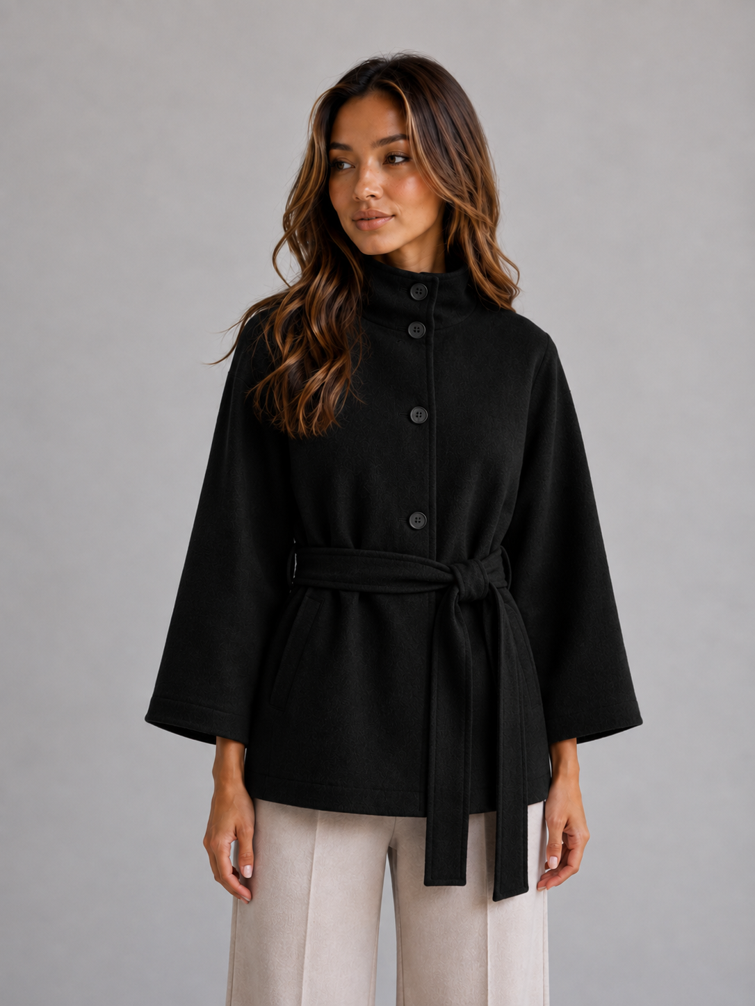 Black version of the belted cape jacket shown from the front, with visible buttons, stand collar, and wide three-quarter sleeves.