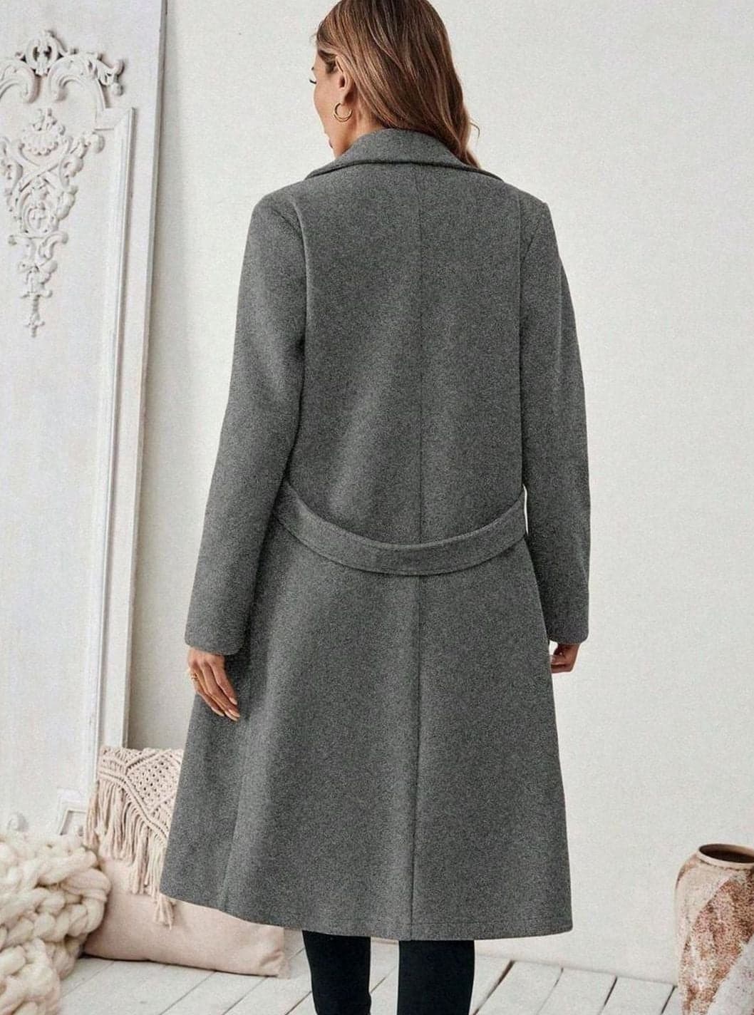 Woman wearing a long notch lapel coat with a buttoned waist tab, welt pockets and long sleeves, holding a quilted handbag._14