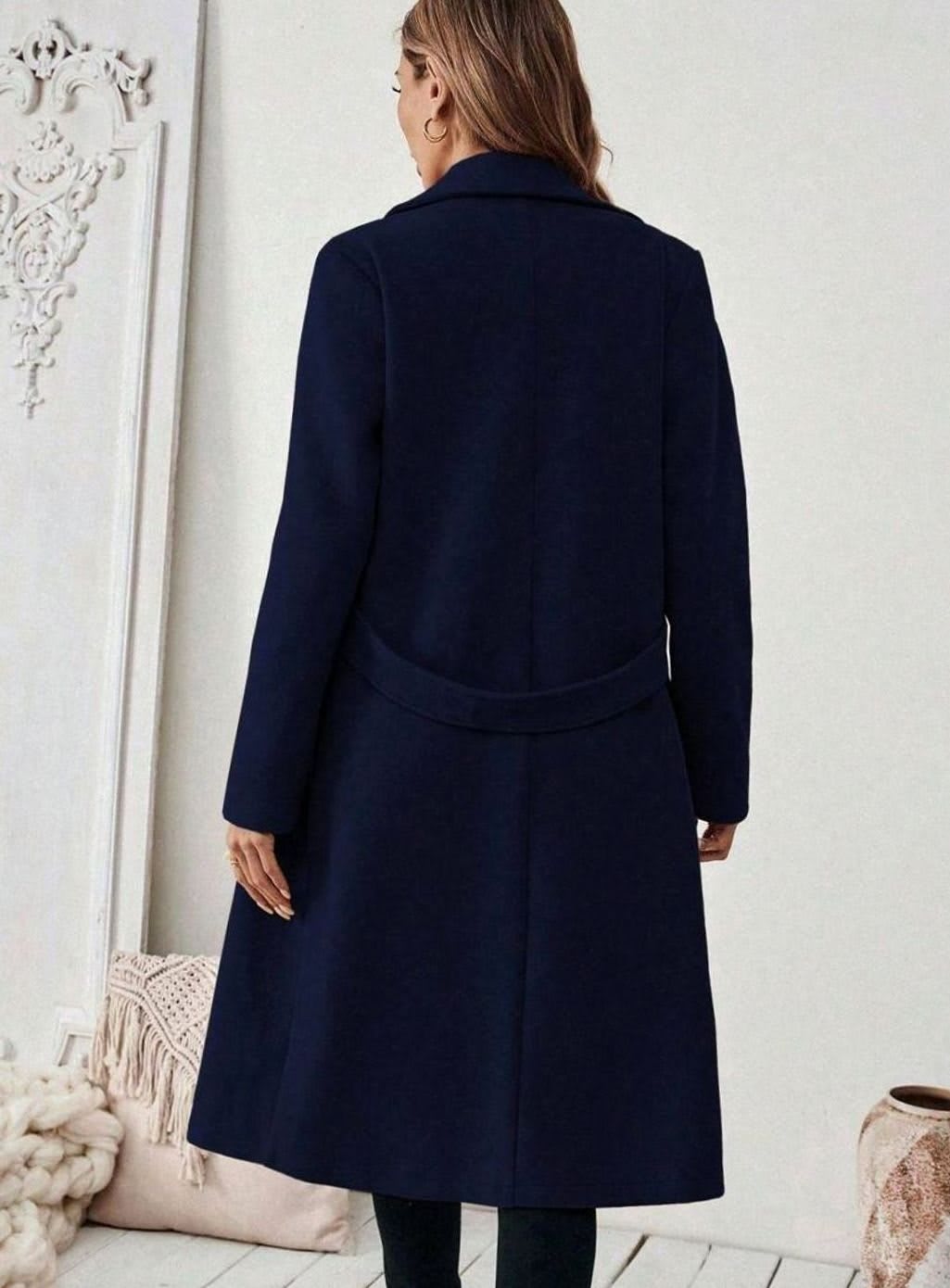 Woman wearing a long notch lapel coat with a buttoned waist tab, welt pockets and long sleeves, holding a quilted handbag._18
