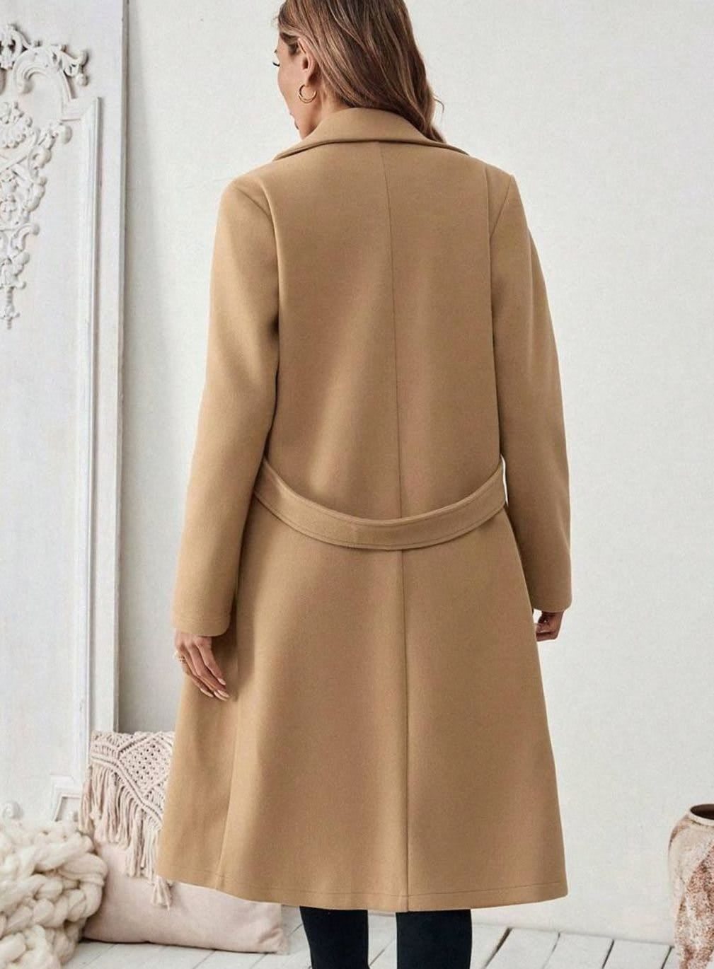 Woman wearing a long notch lapel coat with a buttoned waist tab, welt pockets and long sleeves, holding a quilted handbag._2