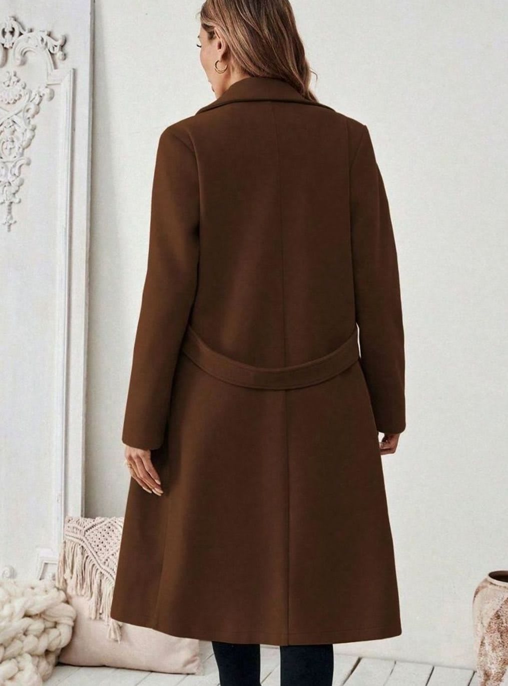 Woman wearing a long notch lapel coat with a buttoned waist tab, welt pockets and long sleeves, holding a quilted handbag._6
