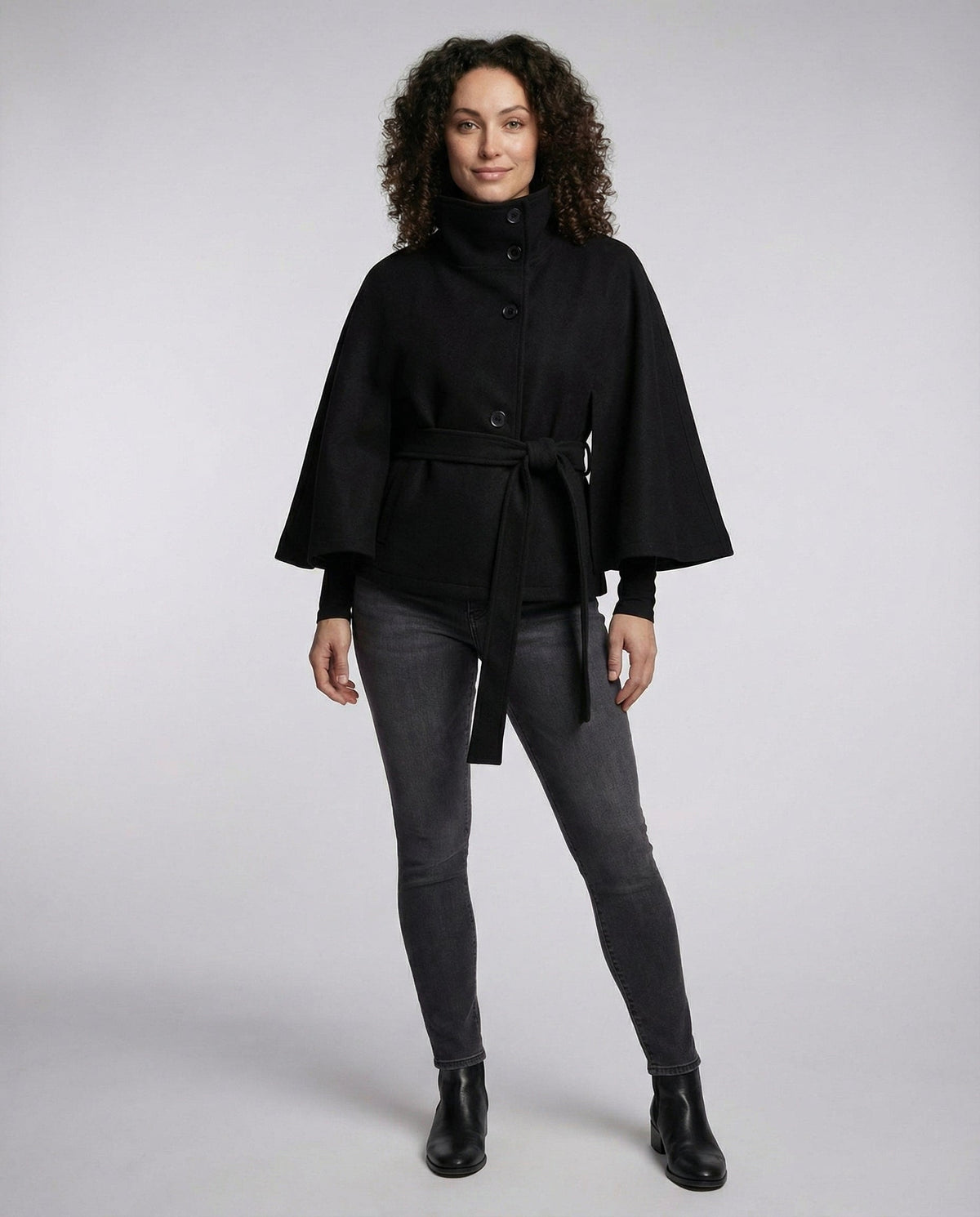 Full-length view of the black wrap jacket styled with slim trousers and ankle boots, showing its relaxed belted silhouette.