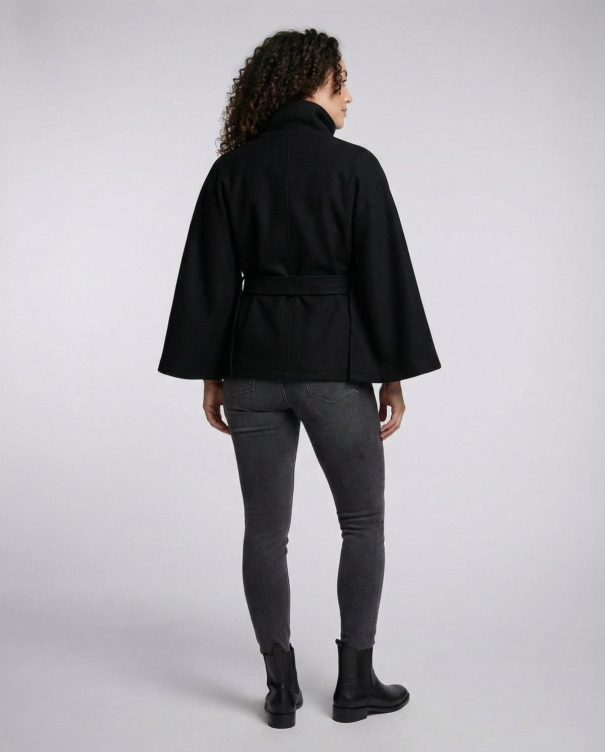 Back view of the black belted jacket showing the relaxed shape, wide sleeves, and waist tie across the back.