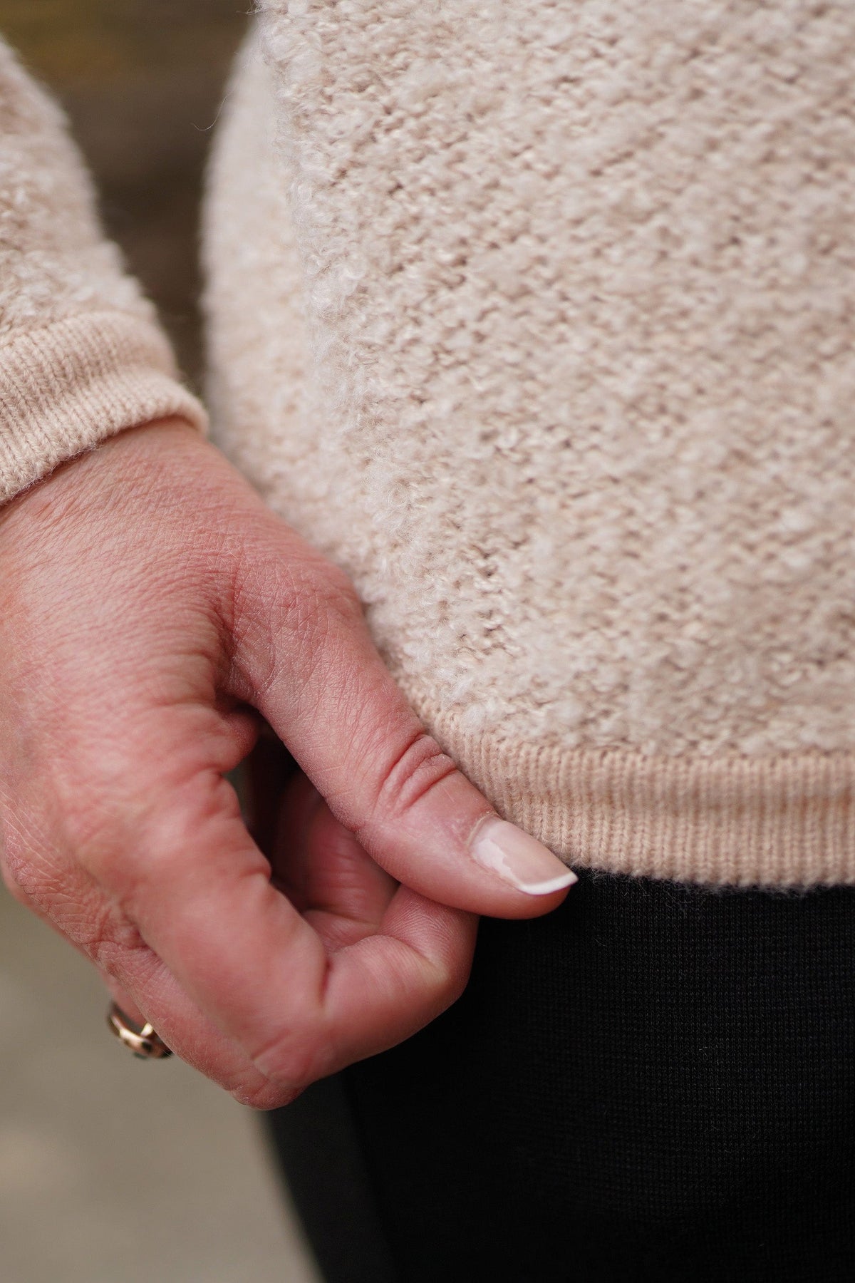 Woman sitting by a brick fireplace holding a cup, wearing a long textured button front cardigan with round neck and ribbed cuffs over jeans._7