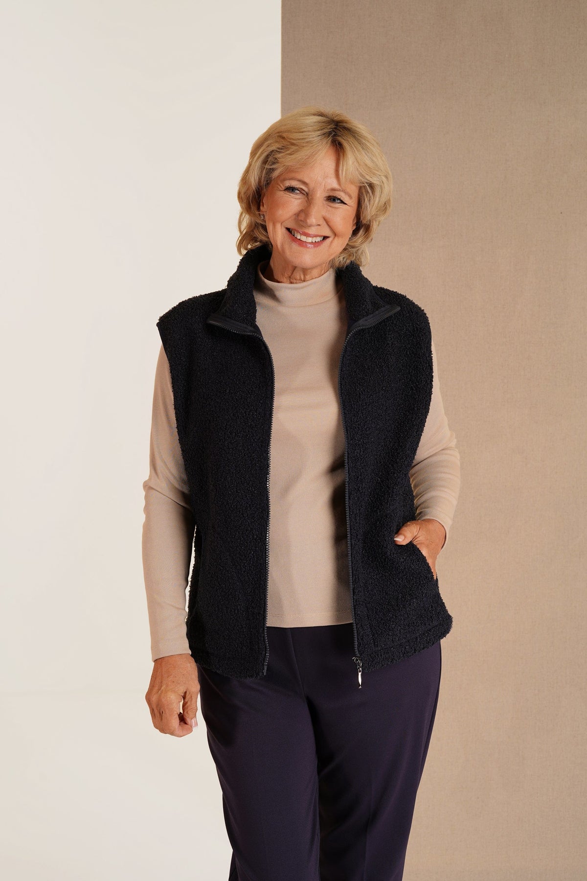 Woman wearing a sleeveless textured zip-front gilet with a stand collar and side pockets over a long-sleeved top and trousers._0