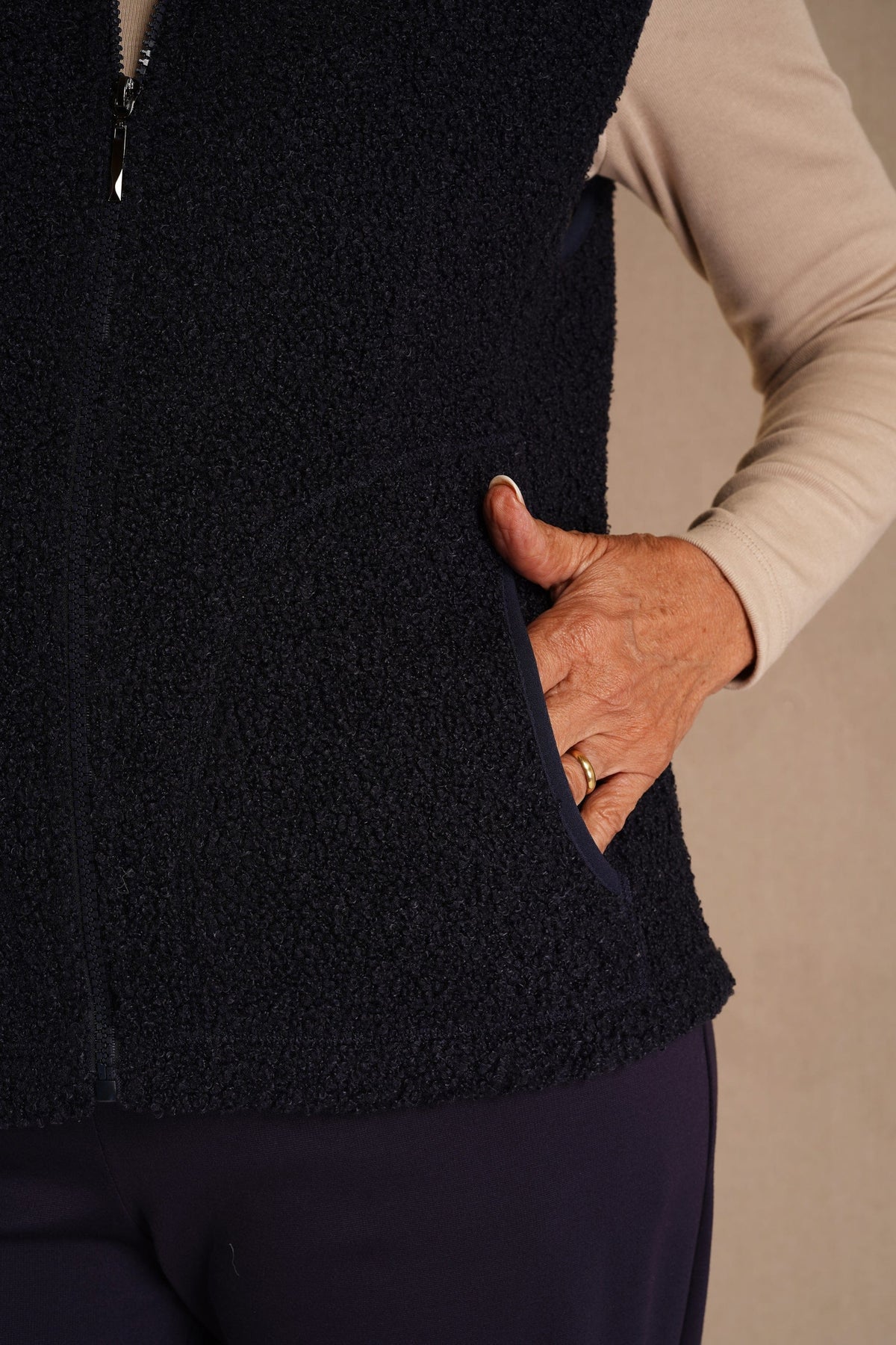 Woman wearing a sleeveless textured zip-front gilet with a stand collar and side pockets over a long-sleeved top and trousers._2