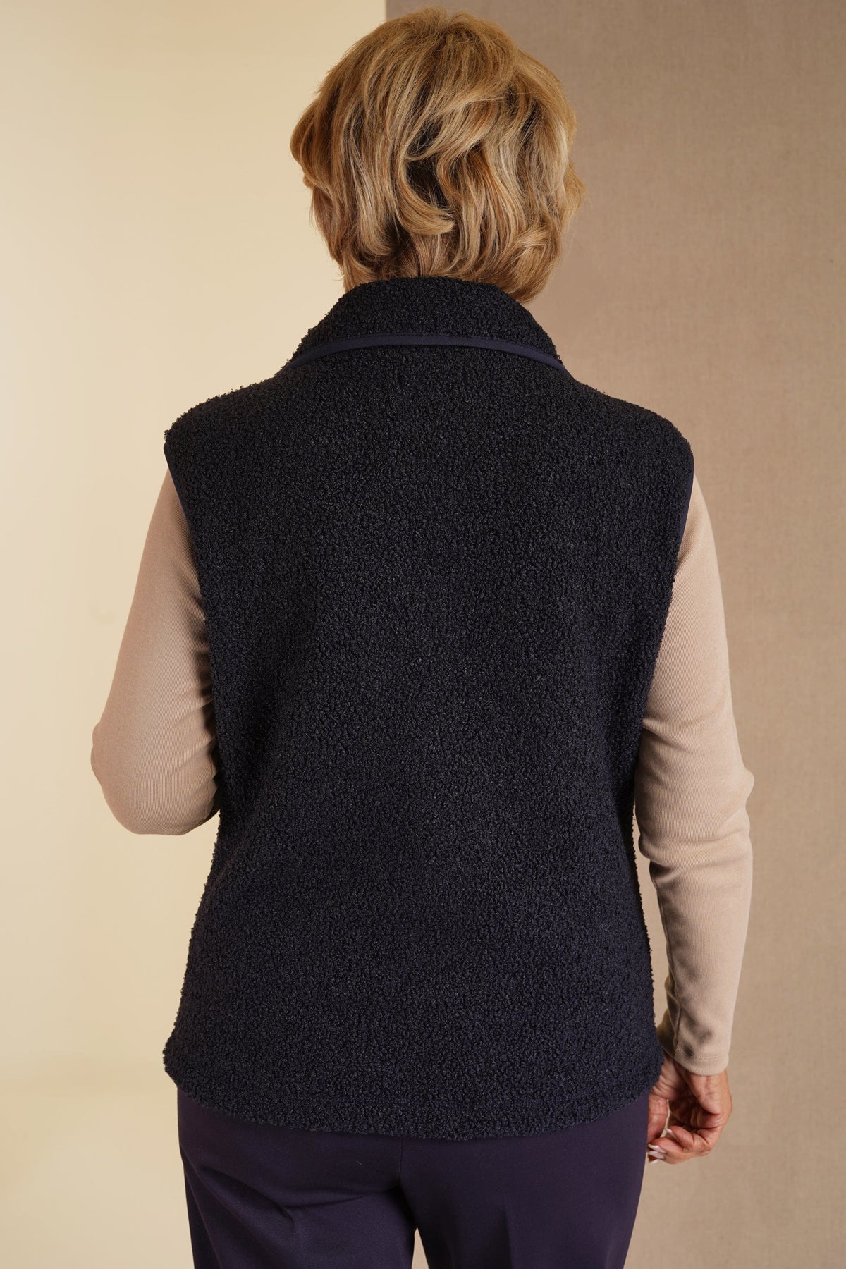 Woman wearing a sleeveless textured zip-front gilet with a stand collar and side pockets over a long-sleeved top and trousers._3