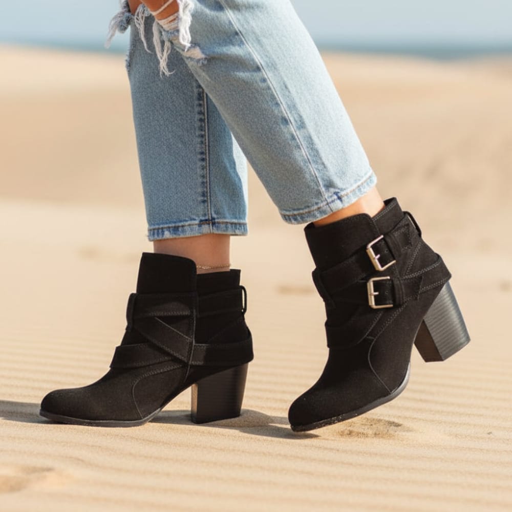 Woman wearing black ankle boots with double buckle straps and block heels, styled with cropped jeans on a beach._0