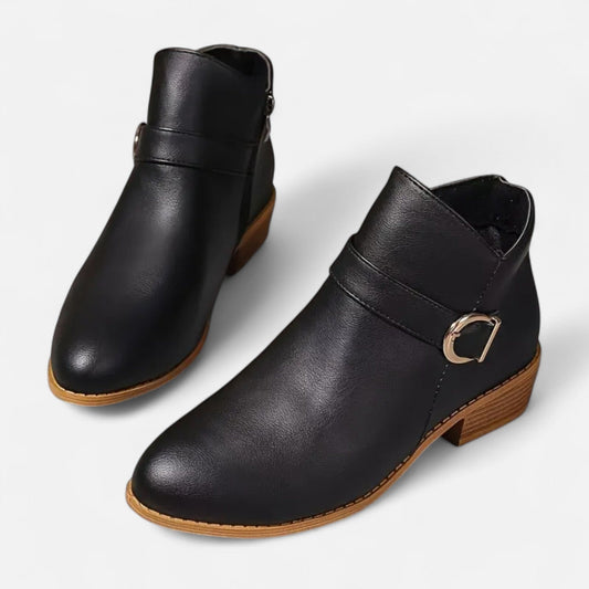 Pair of black ankle boots with smooth rounded toes, side buckle straps, tan-edged soles, and low stacked heels.