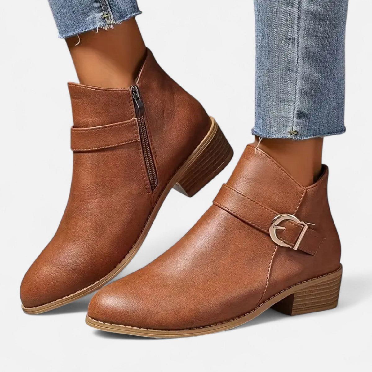 Pair of brown ankle boots with side zippers, buckle straps, tan-edged soles, and low stacked heels worn with cropped jeans.
