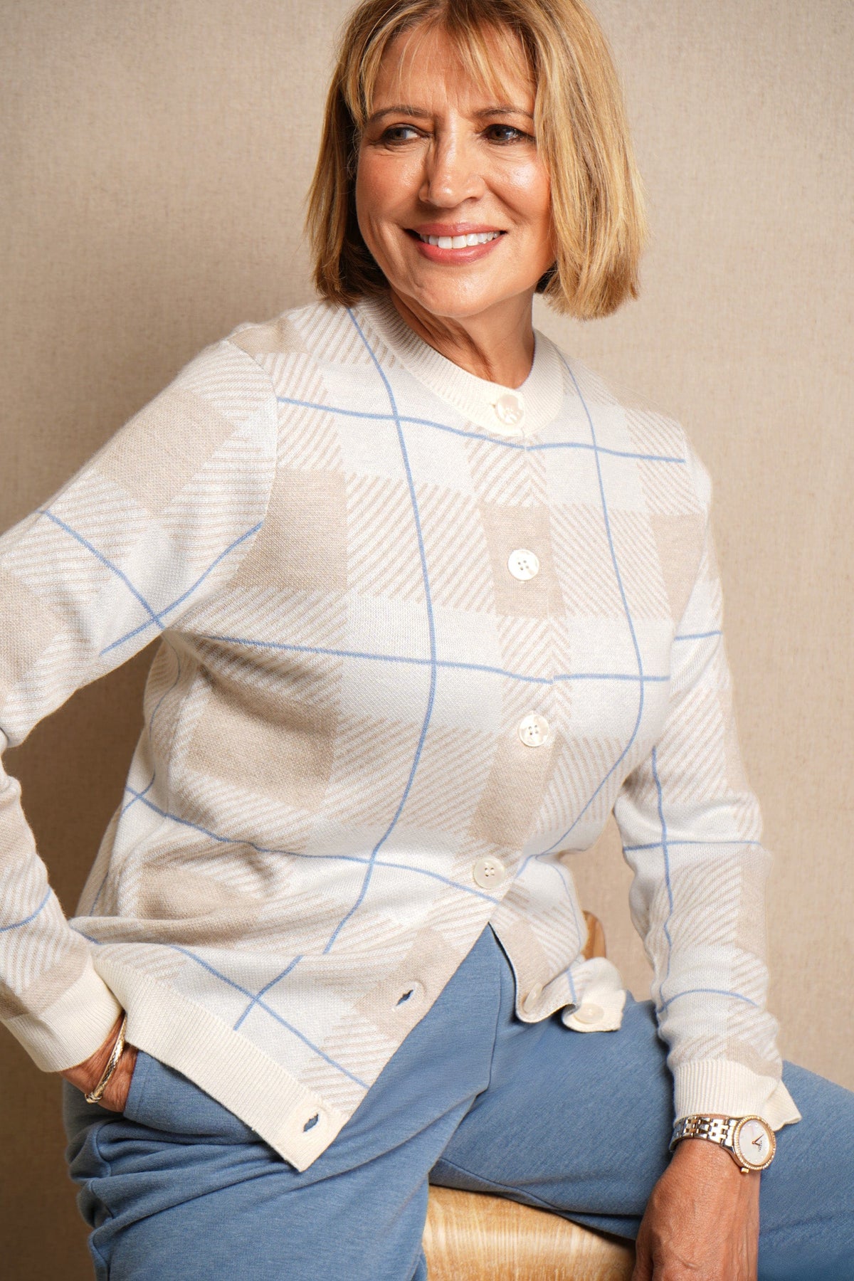 Woman seated wearing a long sleeve button front knit cardigan with a large check pattern and ribbed crew neck, cuffs and hem, with jeans._1