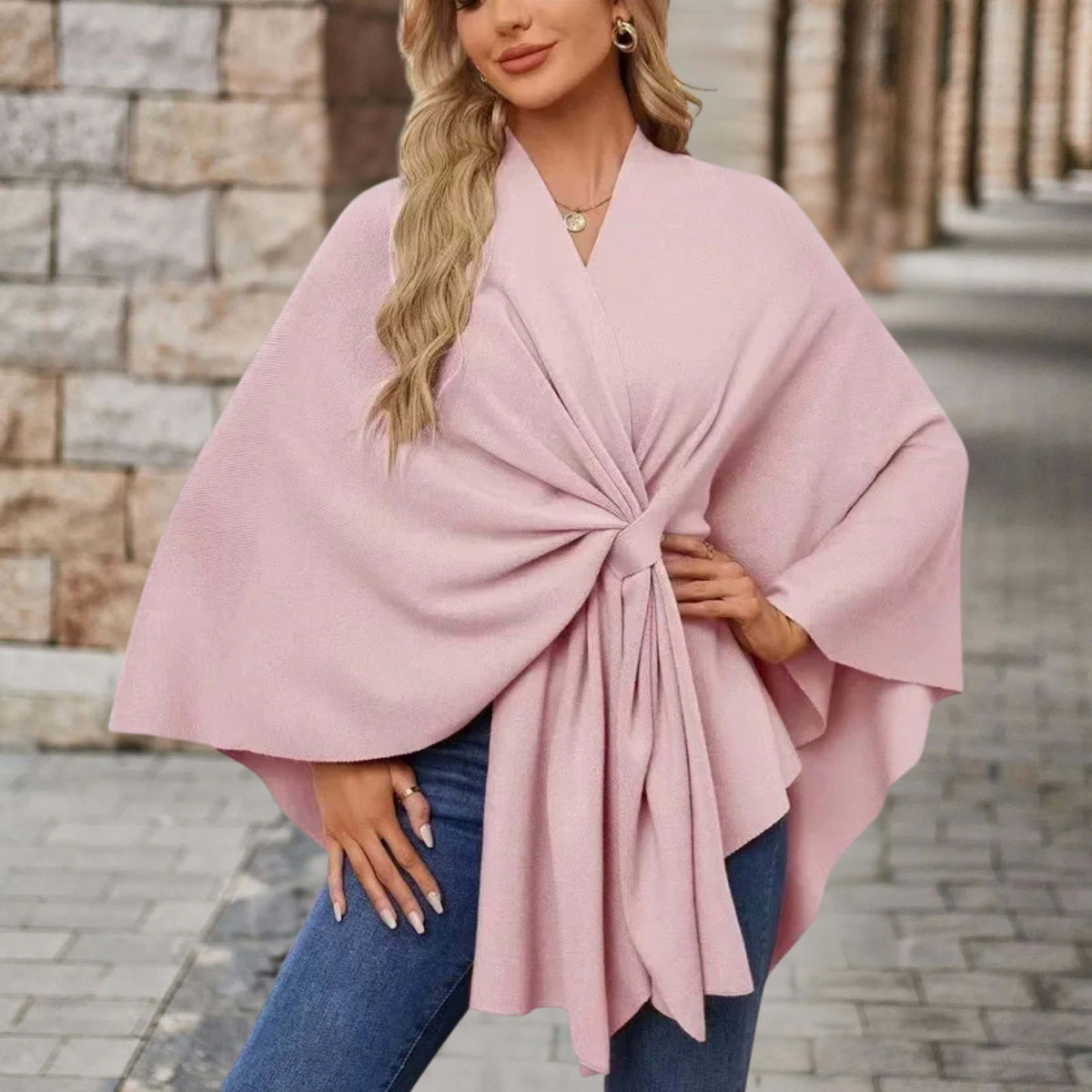 Woman wearing a draped cape style poncho top with a twist tie front and wide sleeves over jeans._0