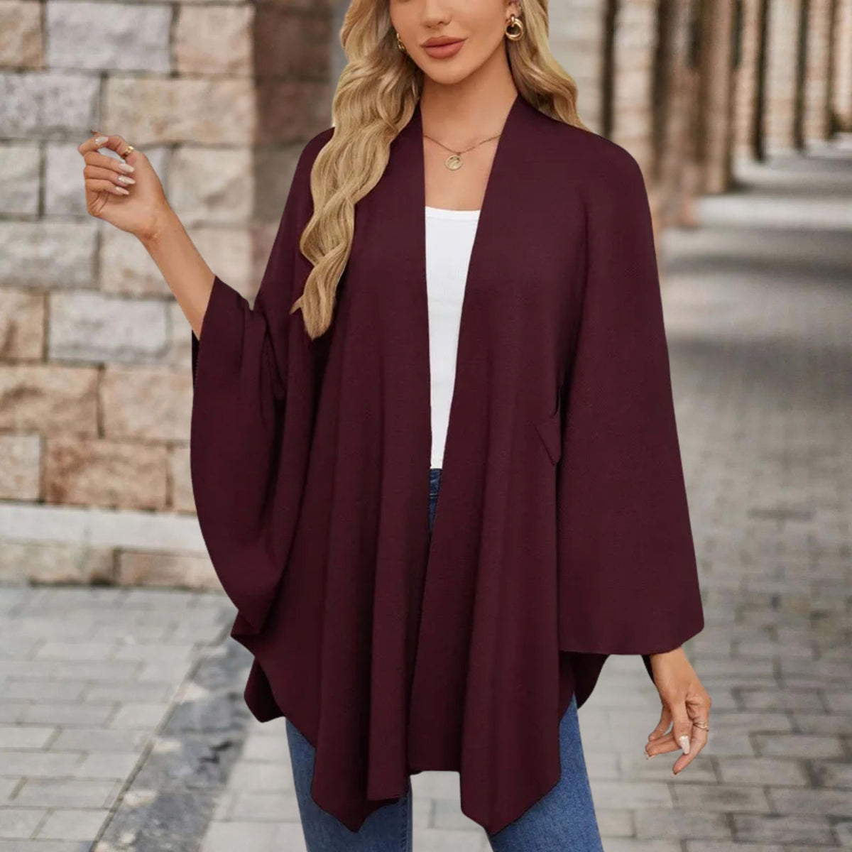 Woman wearing a draped cape style poncho top with a twist tie front and wide sleeves over jeans._11