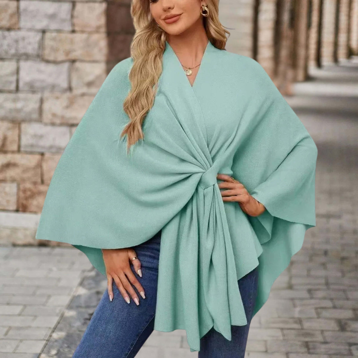 Woman wearing a draped cape style poncho top with a twist tie front and wide sleeves over jeans._9