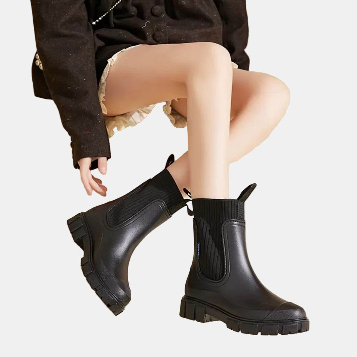 Model wearing black ankle-height Chelsea boots with elastic side panels and chunky treaded soles, paired with a short skirt.