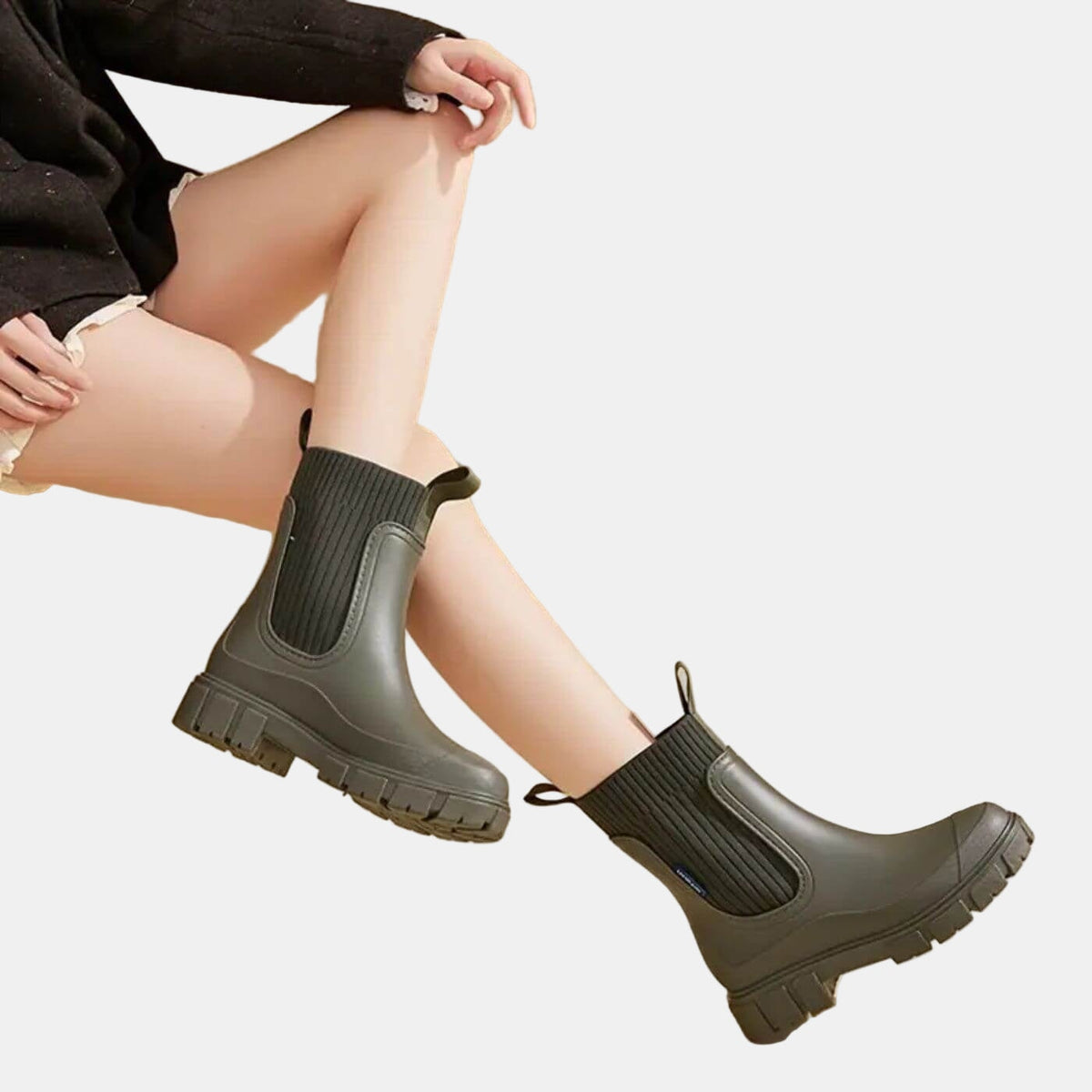 Model seated while wearing black Chelsea boots, with the side panels and heavy lugged soles visible from a diagonal view.