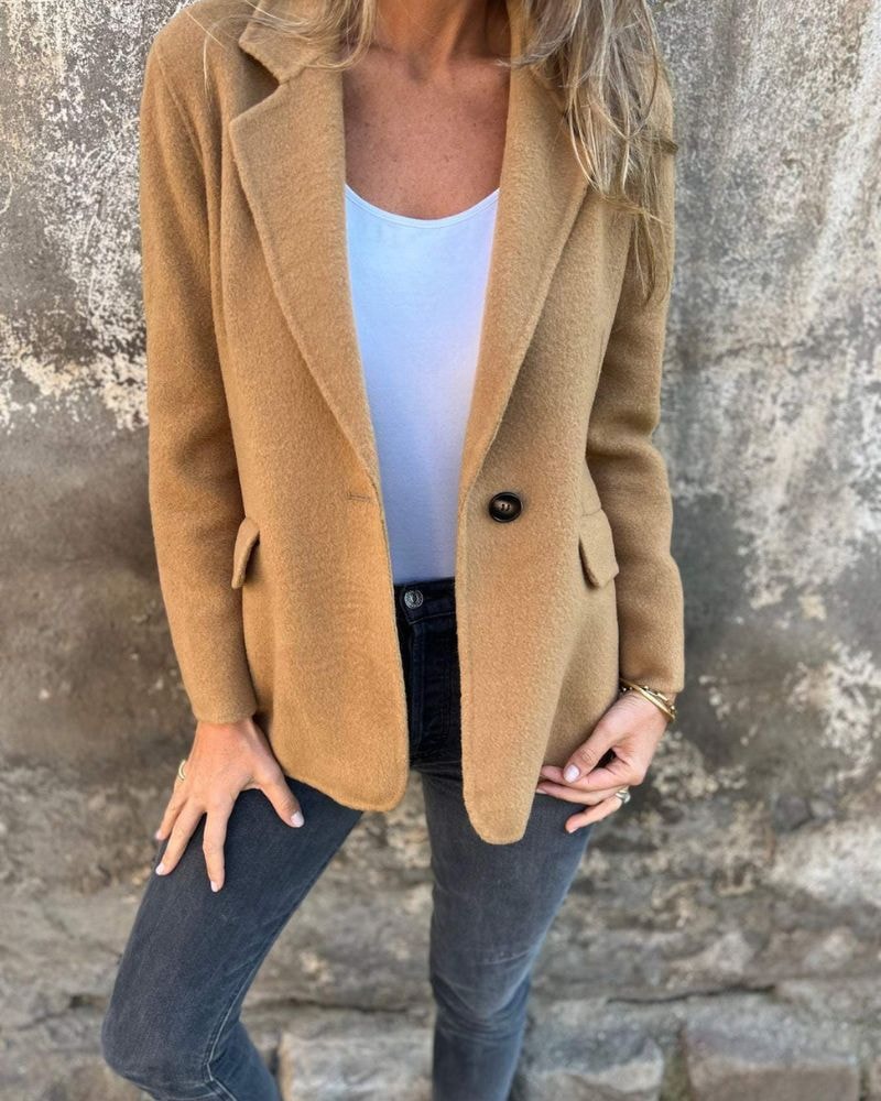 Warm tan blazer jacket with a single-button closure, notched lapels, and flap pockets over a white top.