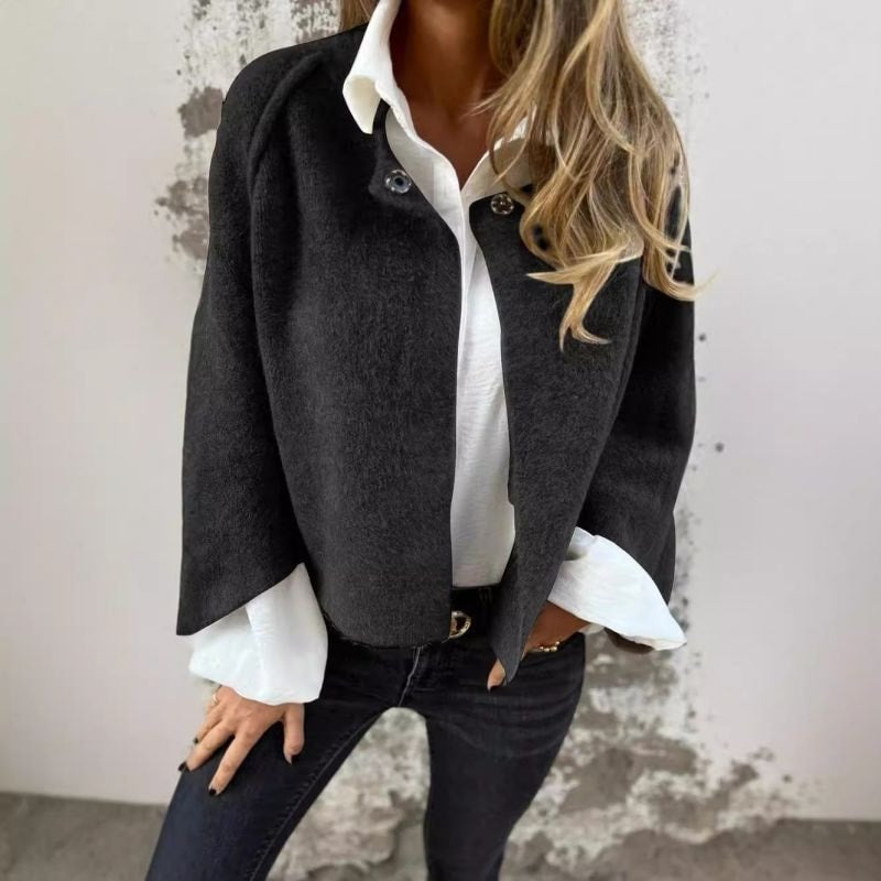 Black collarless button-front jacket styled open over a white shirt and dark jeans.