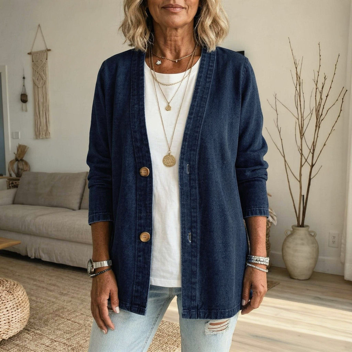 Dark blue denim jacket showing its V-neck, button front, long sleeves, and extended length over a white top.