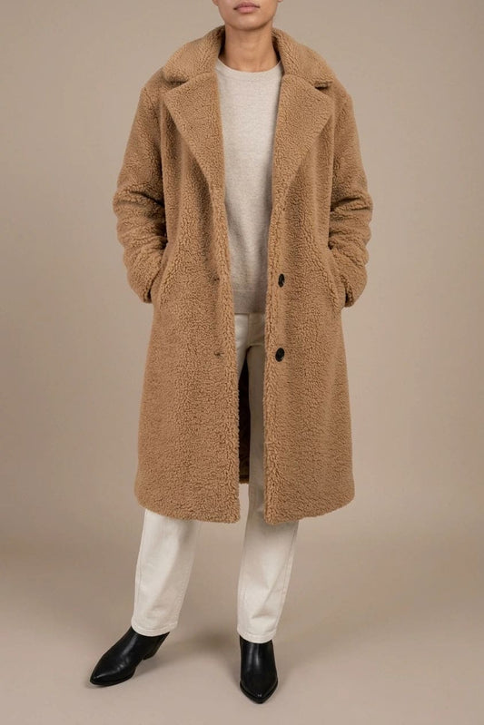 Woman wearing a long textured teddy coat with notch lapels and button front, open over a jumper and trousers with ankle boots._0