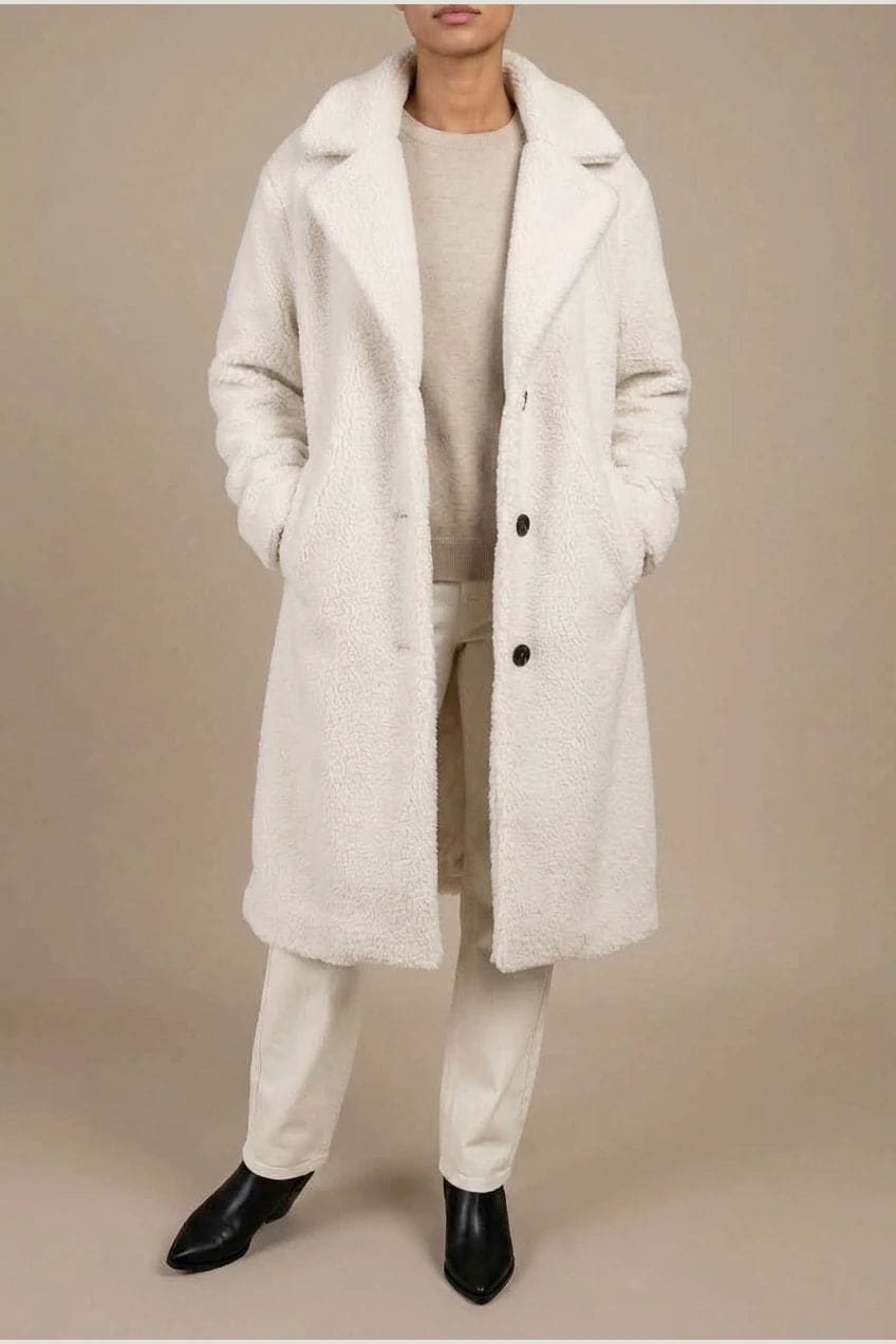 Woman wearing a long textured teddy coat with notch lapels and button front, open over a jumper and trousers with ankle boots._1
