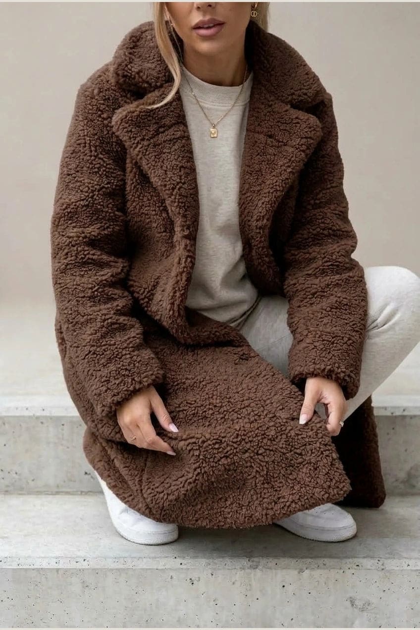 Woman wearing a long textured teddy coat with notch lapels and button front, open over a jumper and trousers with ankle boots._10