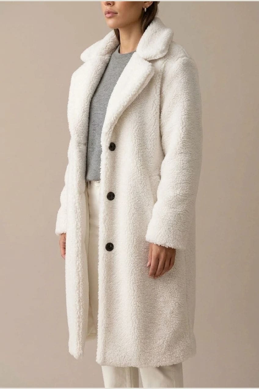 Woman wearing a long textured teddy coat with notch lapels and button front, open over a jumper and trousers with ankle boots._2