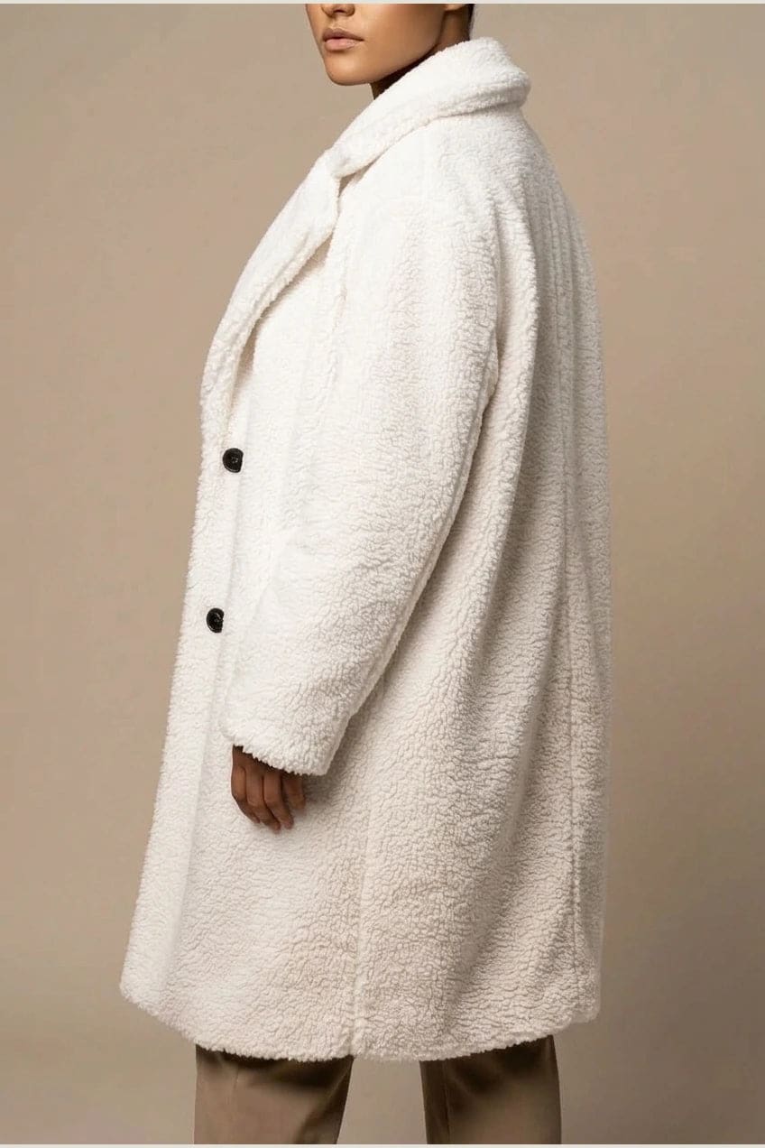Woman wearing a long textured teddy coat with notch lapels and button front, open over a jumper and trousers with ankle boots._3